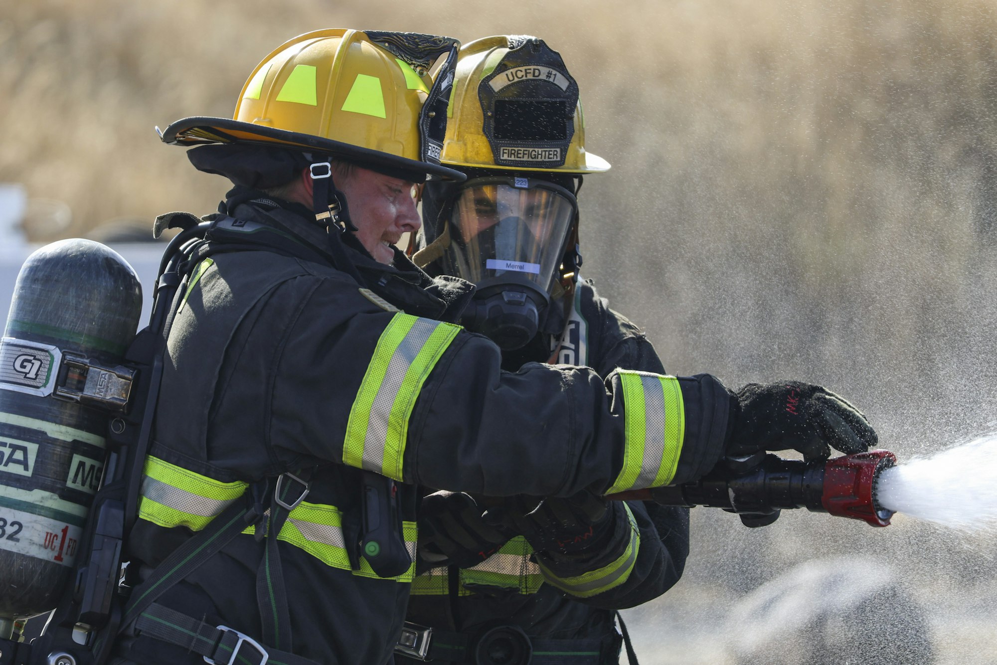 Firefighters spraying water, wearing helmets and protective gear.