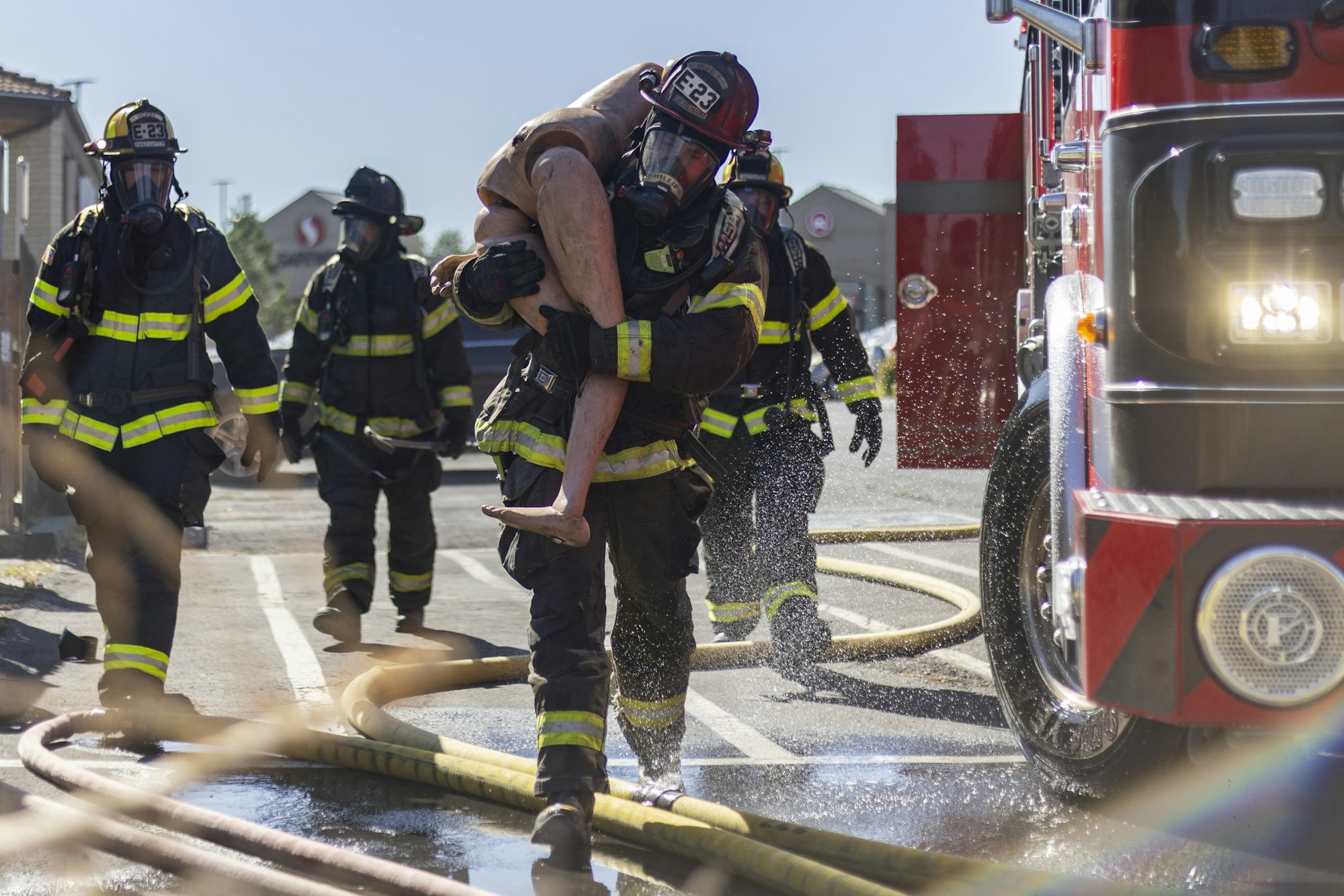 Firefighters carrying a mannequin during a training exercise next to a fire truck.
