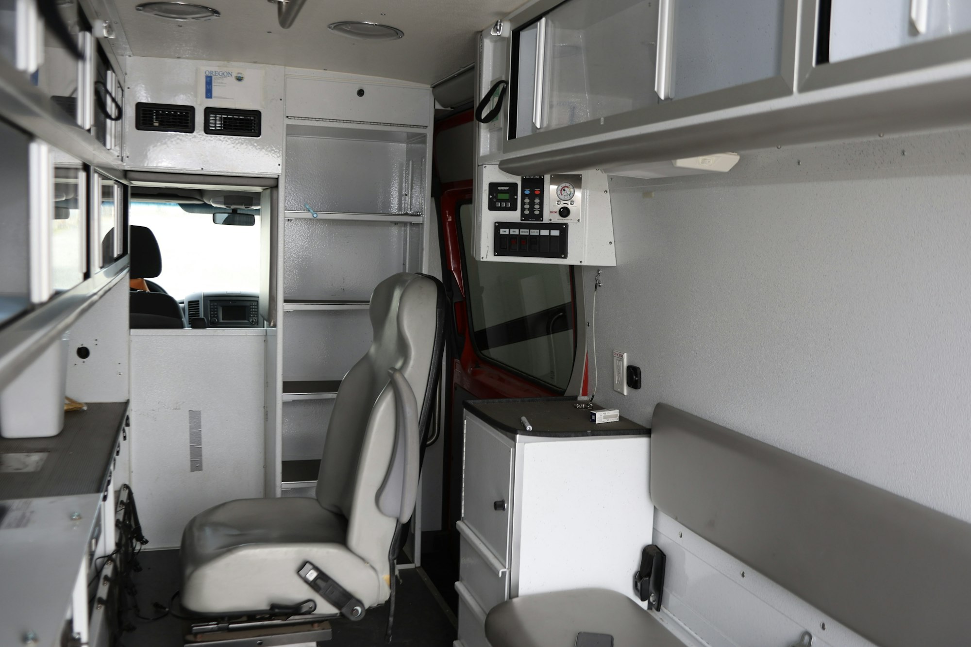 Interior of an empty ambulance showing seats, cabinets, and medical equipment compartments.