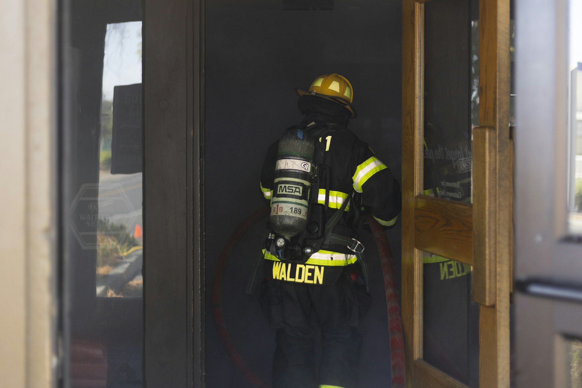 A firefighter in full gear enters a smoky building with a hose.