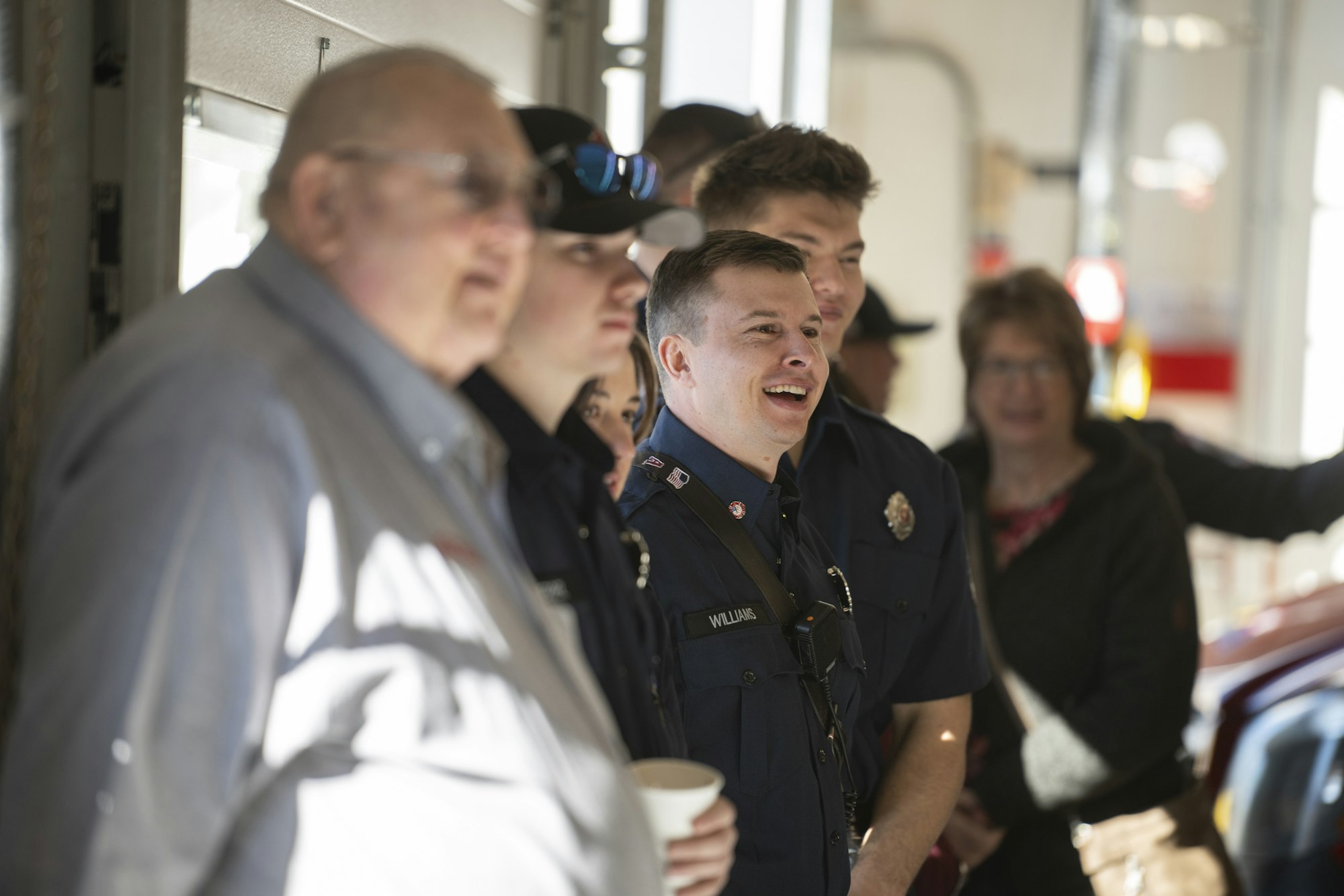 A group of people, some in blue uniforms, stand together indoors, smiling and interacting.