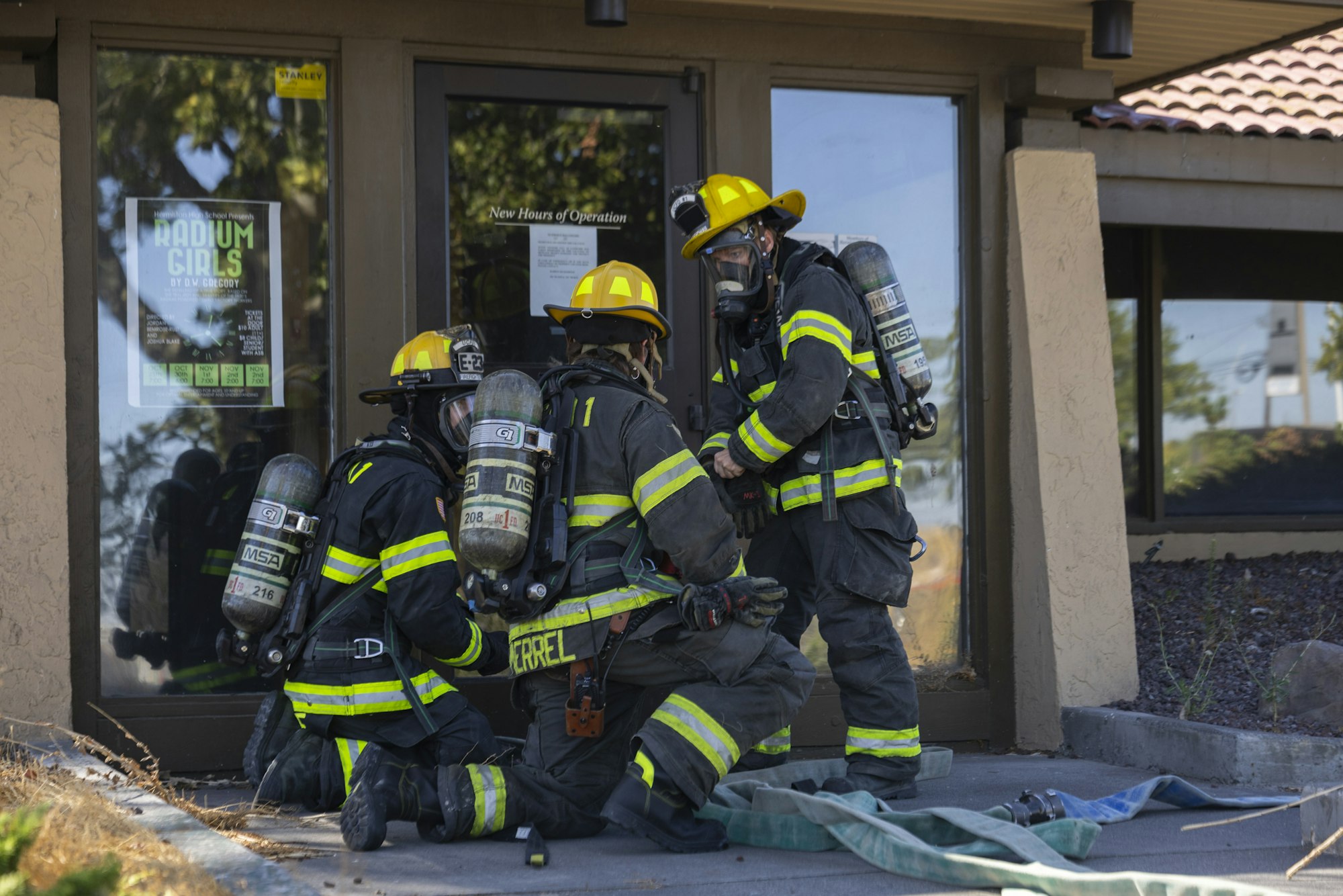 Three firefighters in gear and helmets are preparing hoses outside a building.