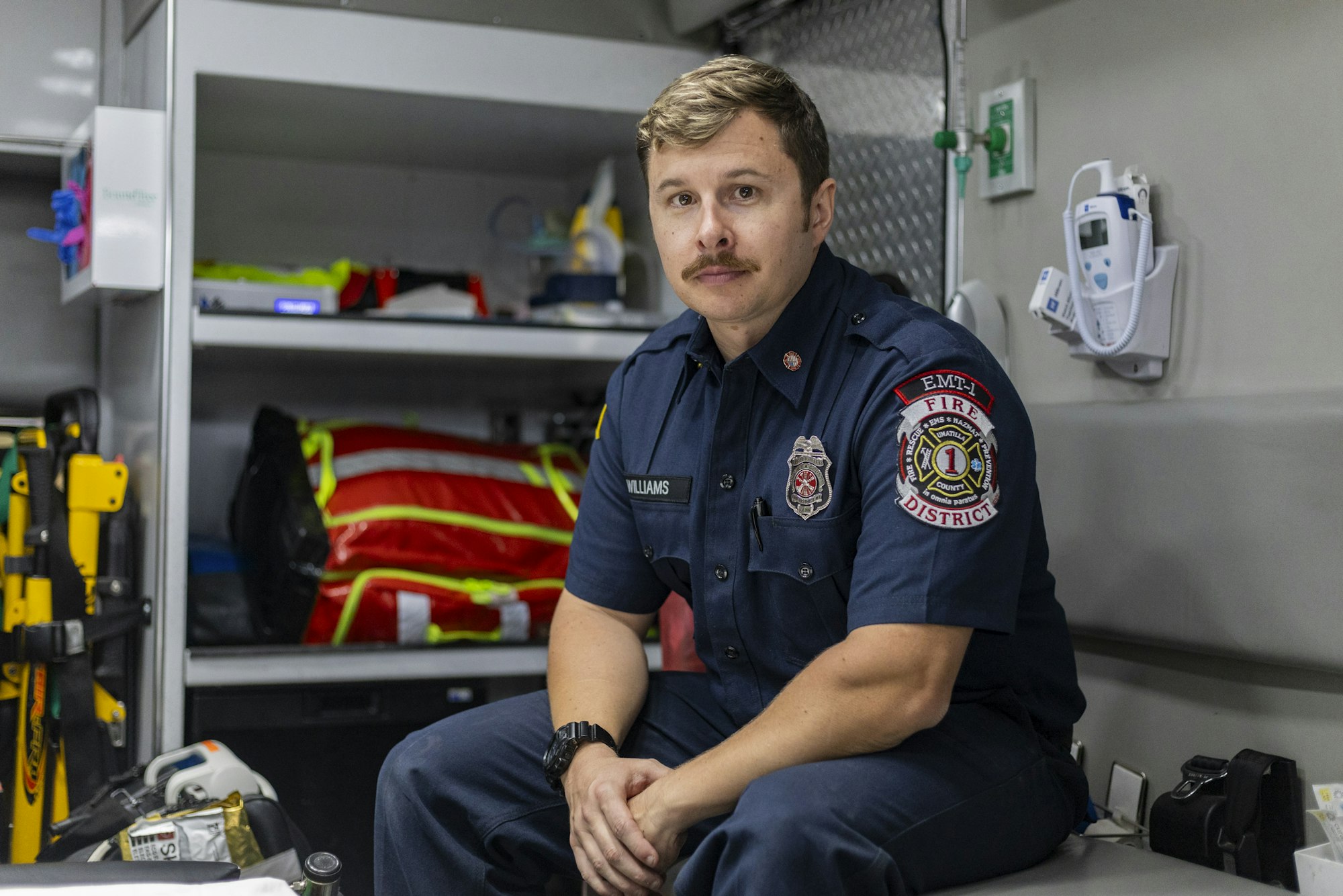 A firefighter in uniform sitting in an ambulance with equipment and medical supplies around.