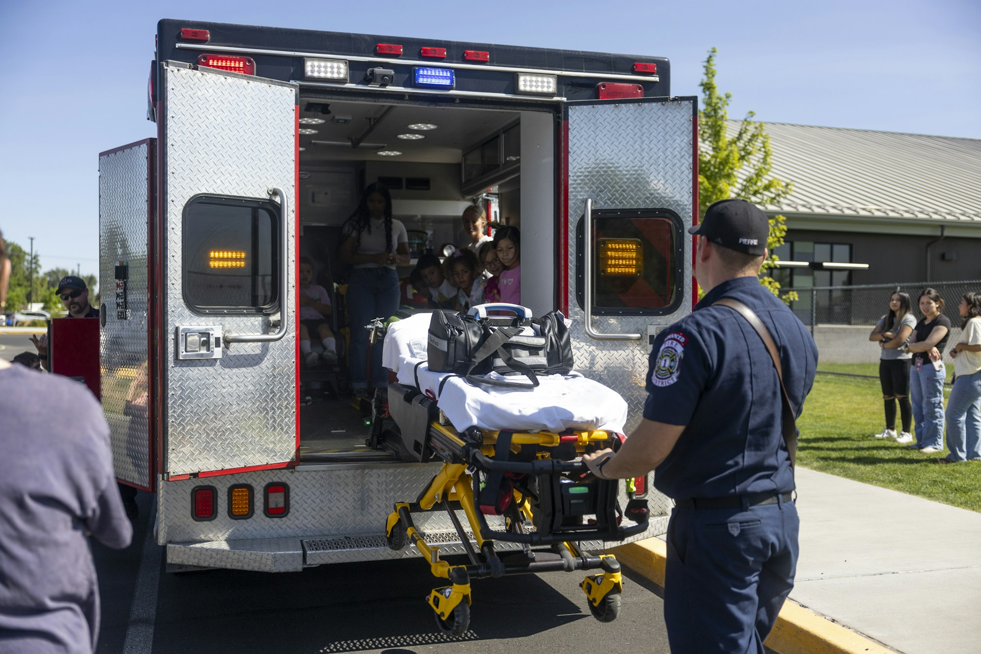 An open ambulance with people inside. A man in uniform, likely a paramedic, is handling a stretcher outside.