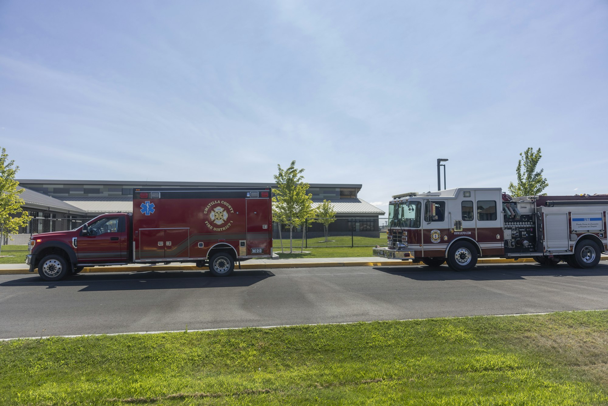 Fire truck and ambulance parked on a road in front of a building, with trees and grass nearby.
