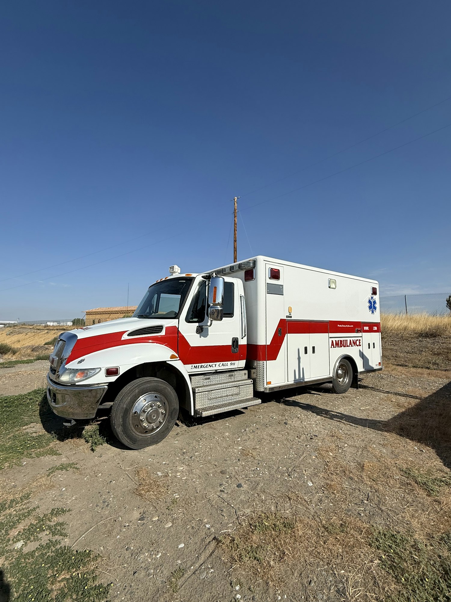 A parked ambulance on a dirt road with a clear blue sky above.