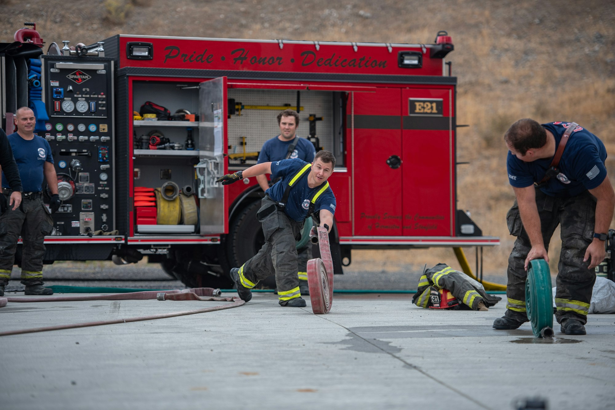 Firefighters engage in hose training near a fire truck labeled "Pride Honor Dedication."