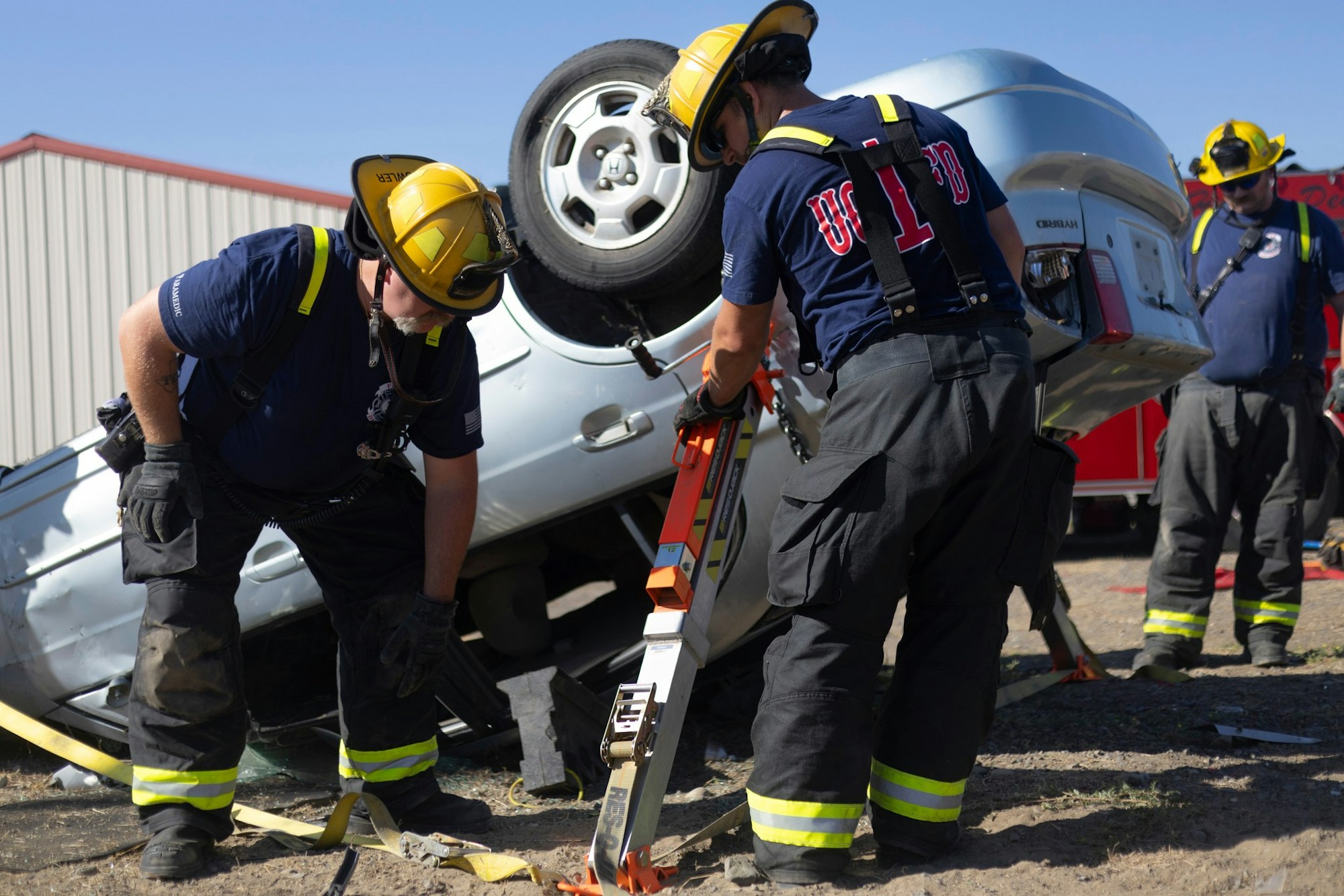 Firefighters stabilize an overturned car with tools at an accident scene.