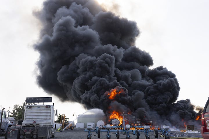 Large dark smoke and flames from a fire near a truck and equipment in an industrial area.