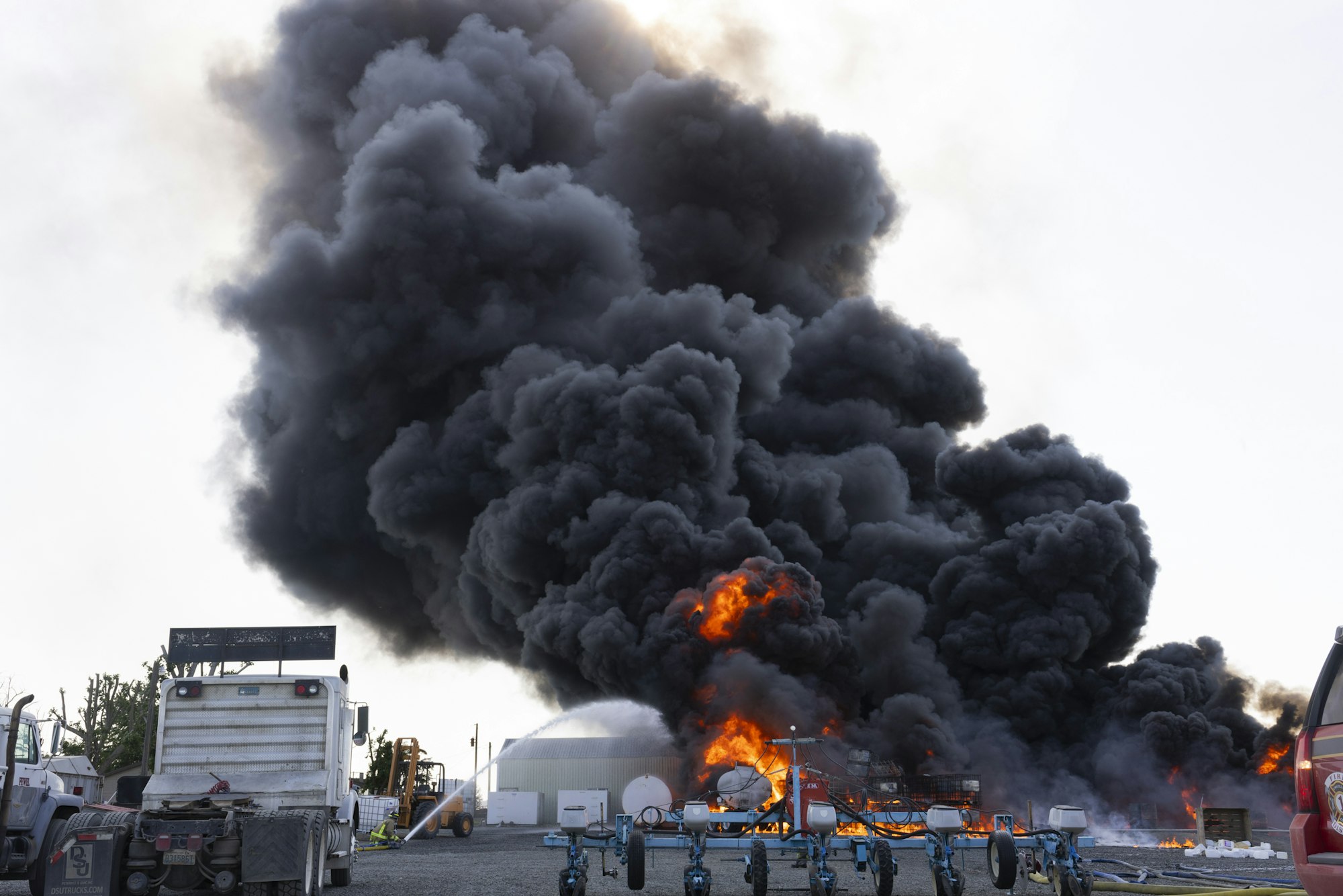 Large dark smoke and flames from a fire near a truck and equipment in an industrial area.