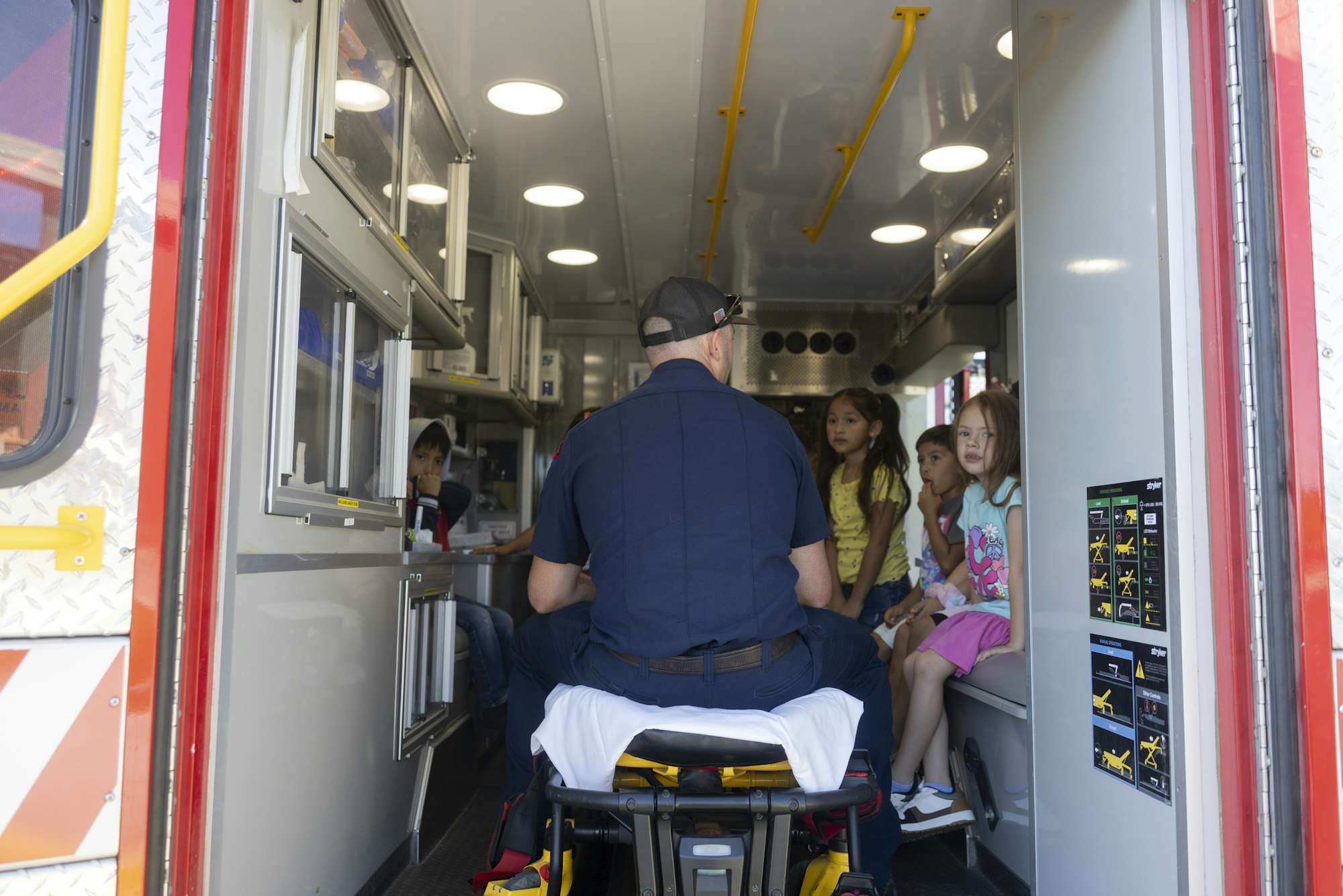 A person in uniform sits inside an ambulance, talking to four children seated inside.