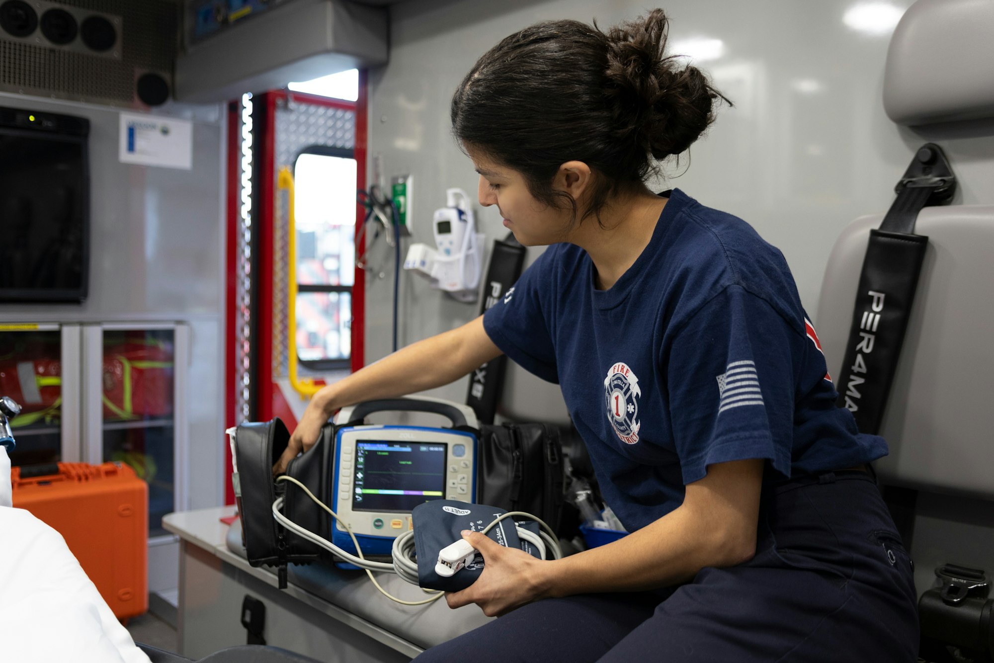 A person in an ambulance uses medical equipment, such as a monitor and blood pressure cuff.