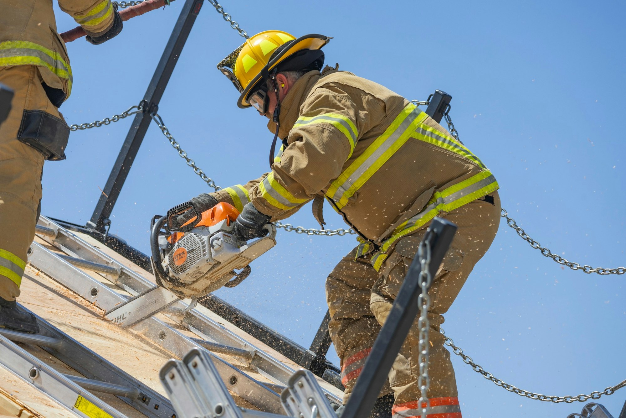 Firefighter in gear using a chainsaw on a roof.