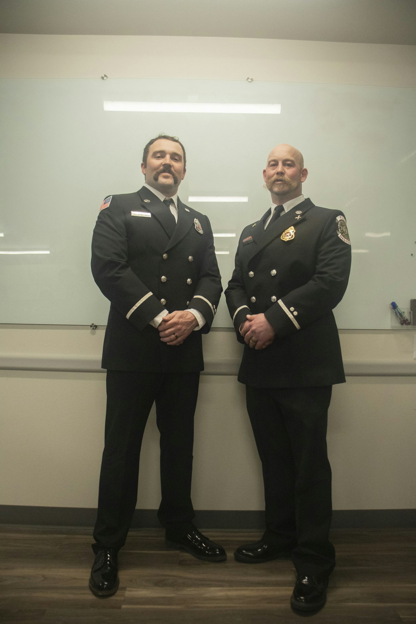 Two men in matching formal uniforms, standing in front of a whiteboard.