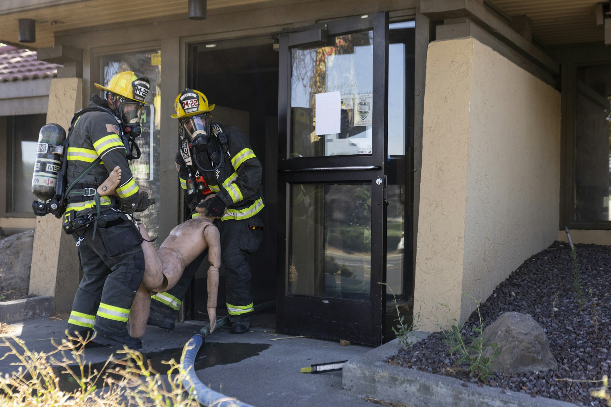 Firefighters in gear carrying a dummy out of a building.