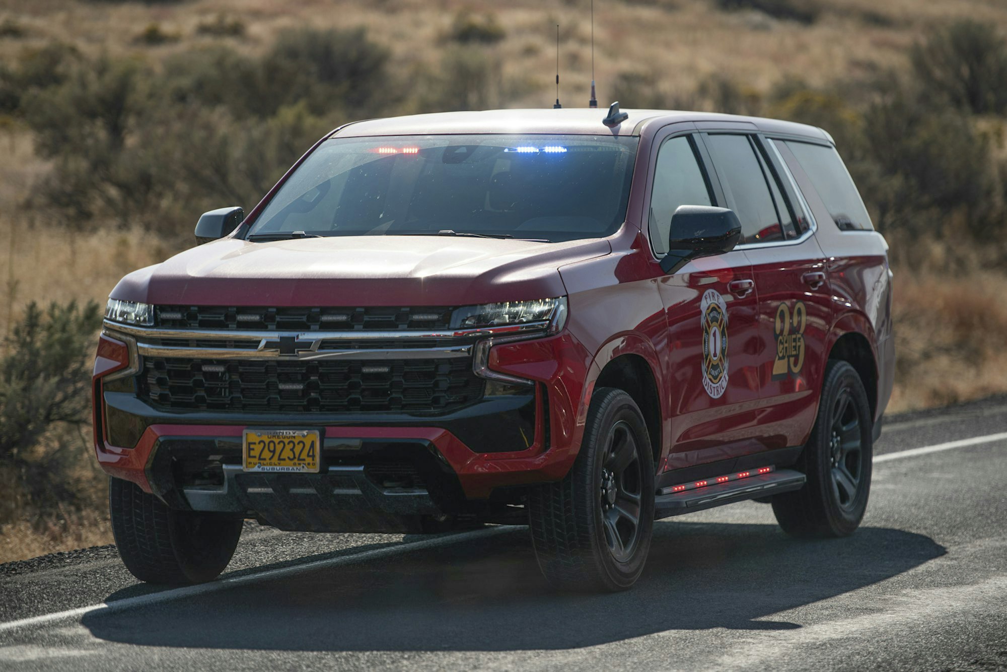 A red emergency vehicle on a road, displaying a "Fire District" insignia and its emergency lights activated.