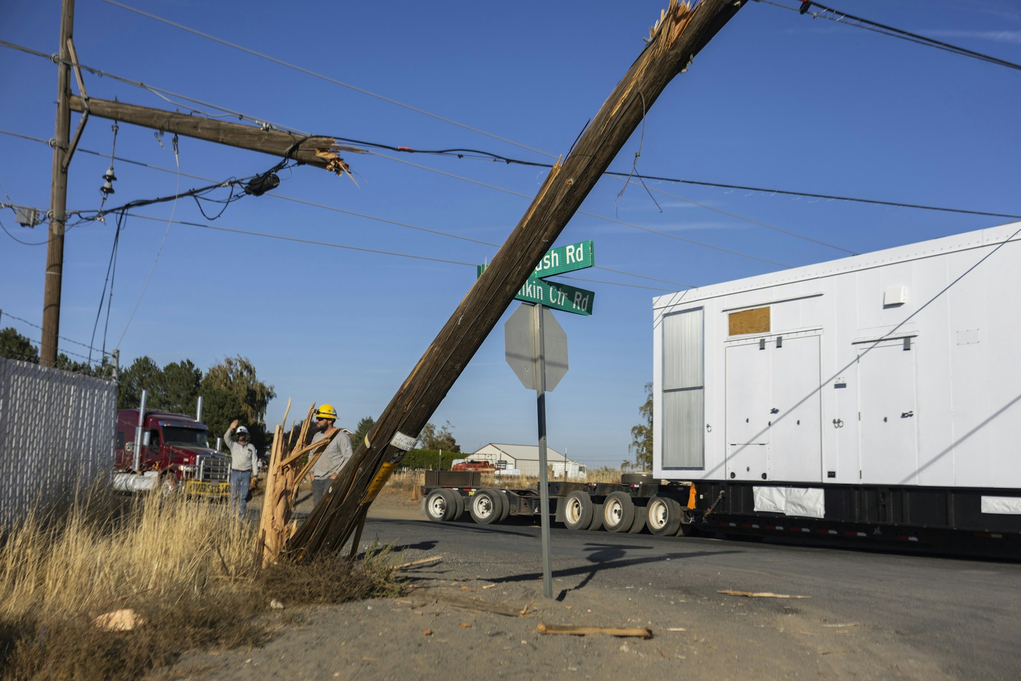 Workers handle a broken utility pole at the corner of Brush Rd and Lincoln Ctr Rd, with a large truck nearby.