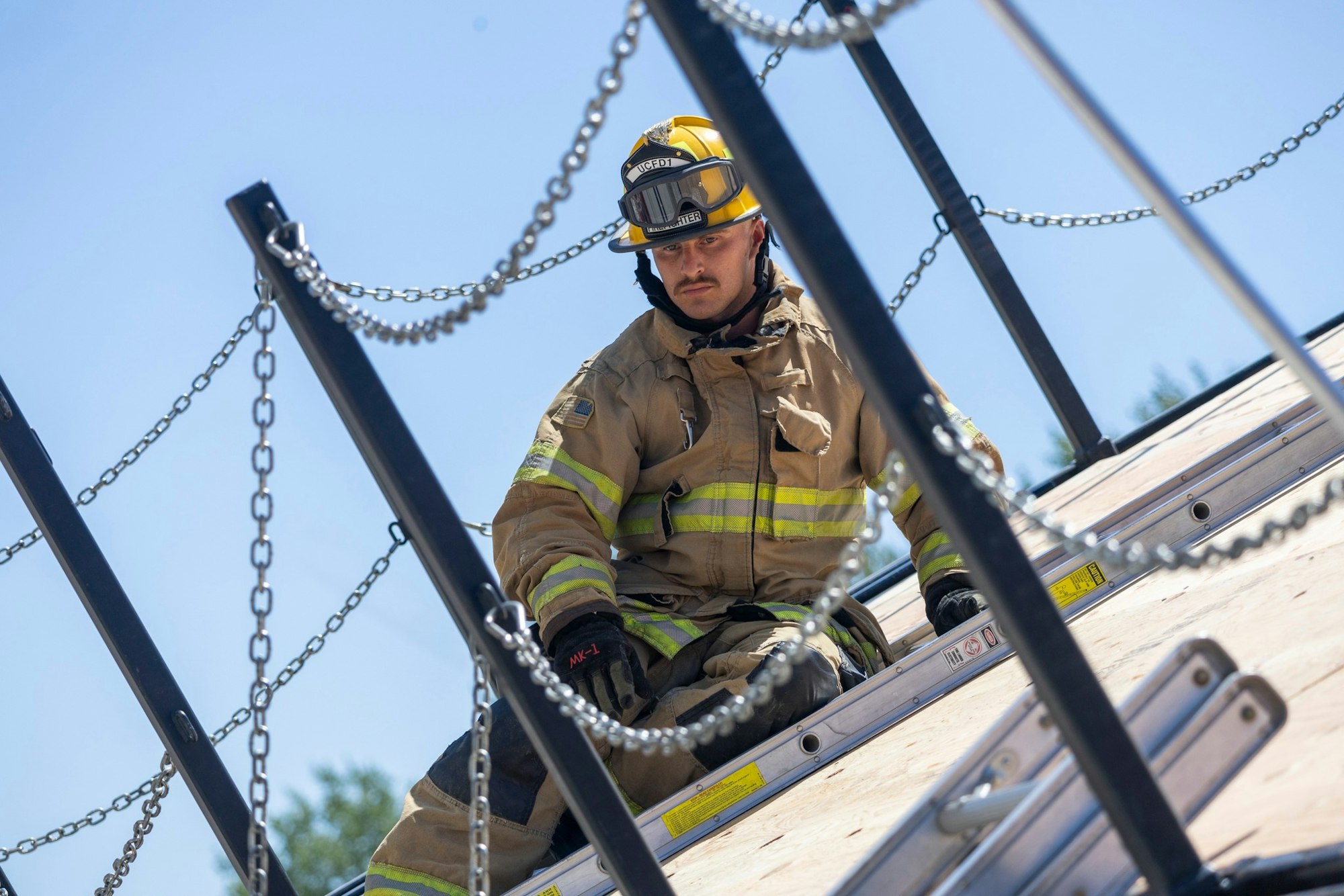 A firefighter in gear on a rooftop, surrounded by chains and metal beams.