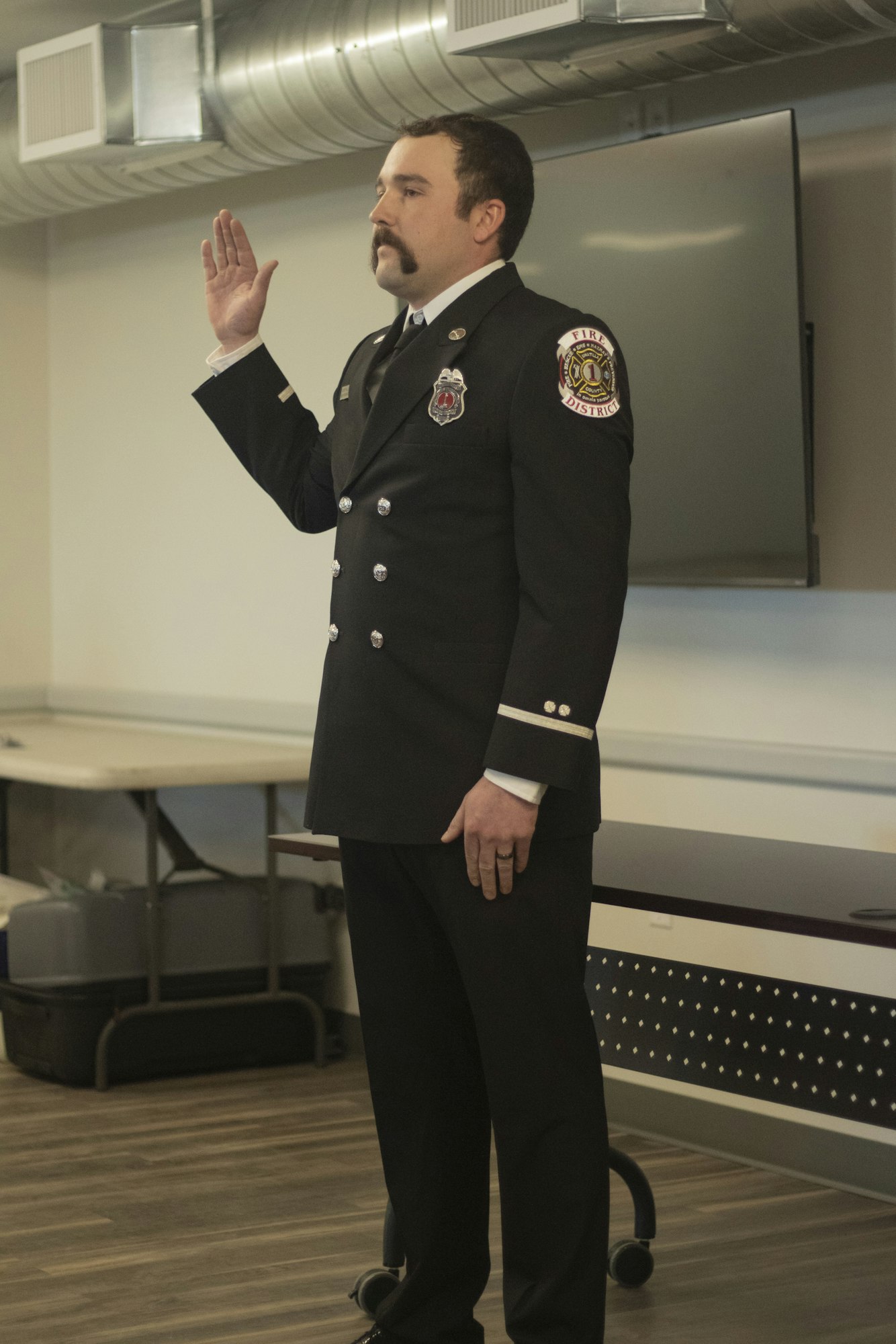 A firefighter in uniform raising their right hand, possibly during a ceremony.