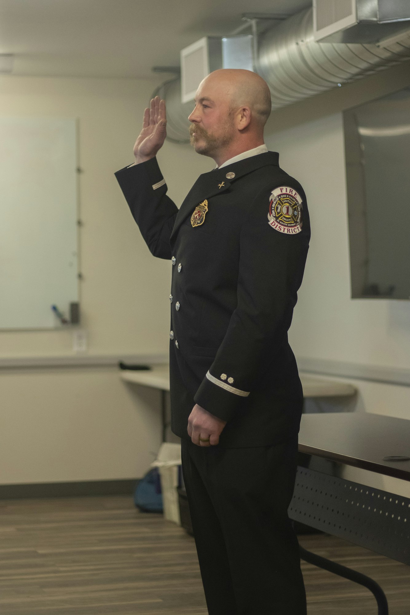 A firefighter in uniform taking an oath with right hand raised in a room.