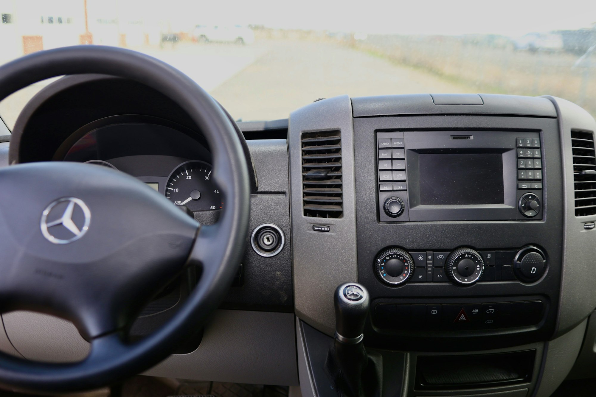 Car dashboard with Mercedes steering wheel, speedometer, center console display, controls, and gear shift.