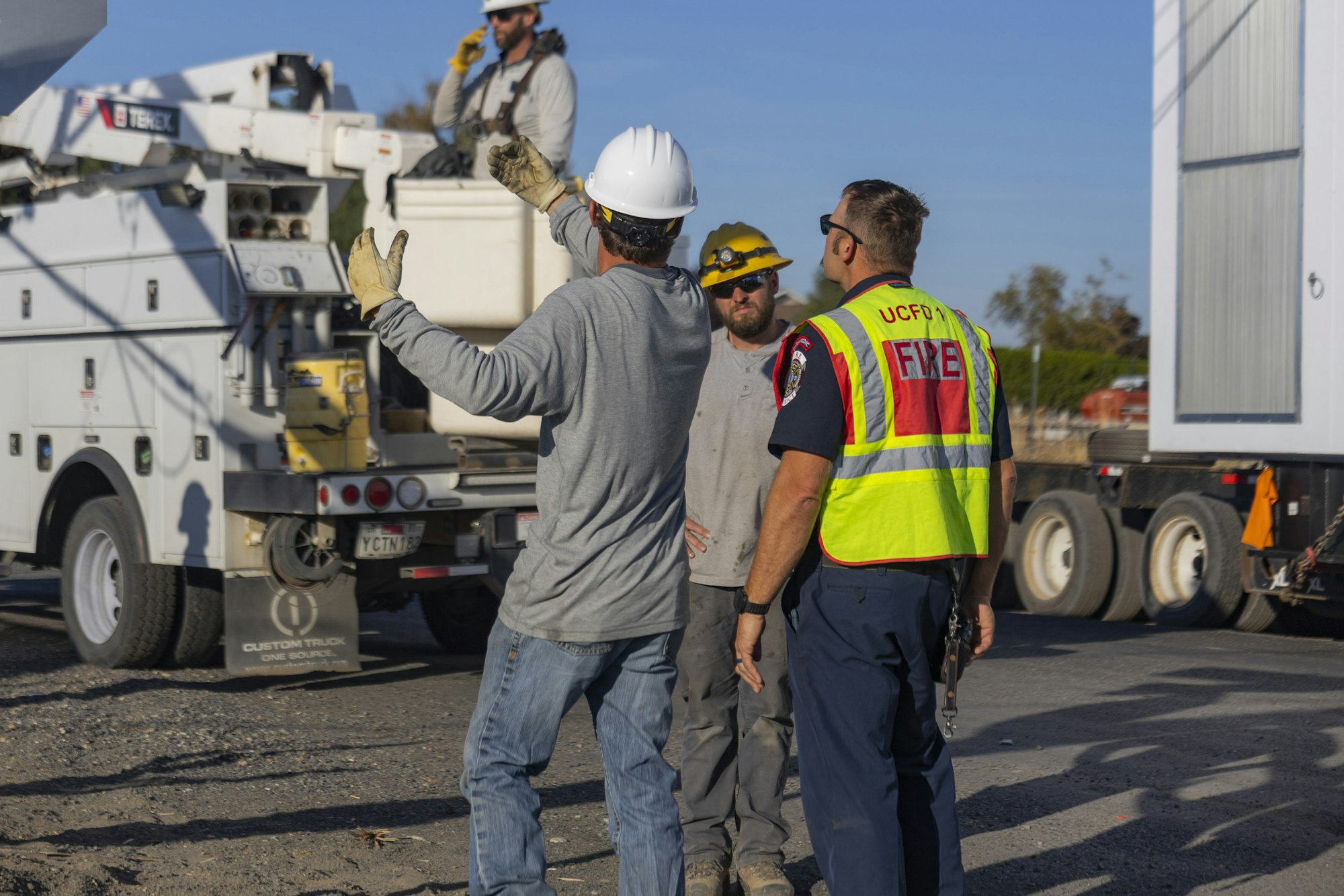 Construction workers and a firefighter discussing near utility trucks.