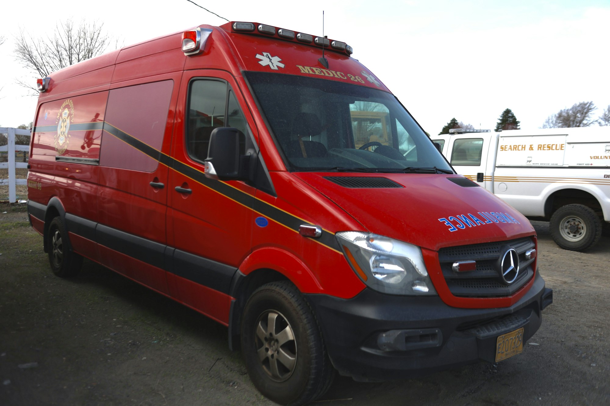 Red ambulance van with “Medic 28” and “Ambulance” marked. Another search and rescue vehicle in the background.