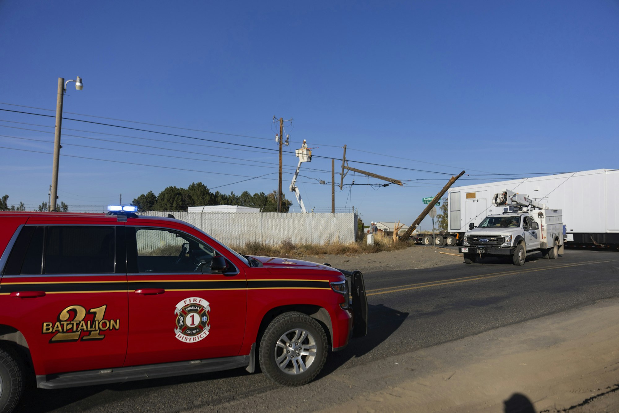 Red fire district vehicle and utility truck at a roadside scene with a damaged power pole.