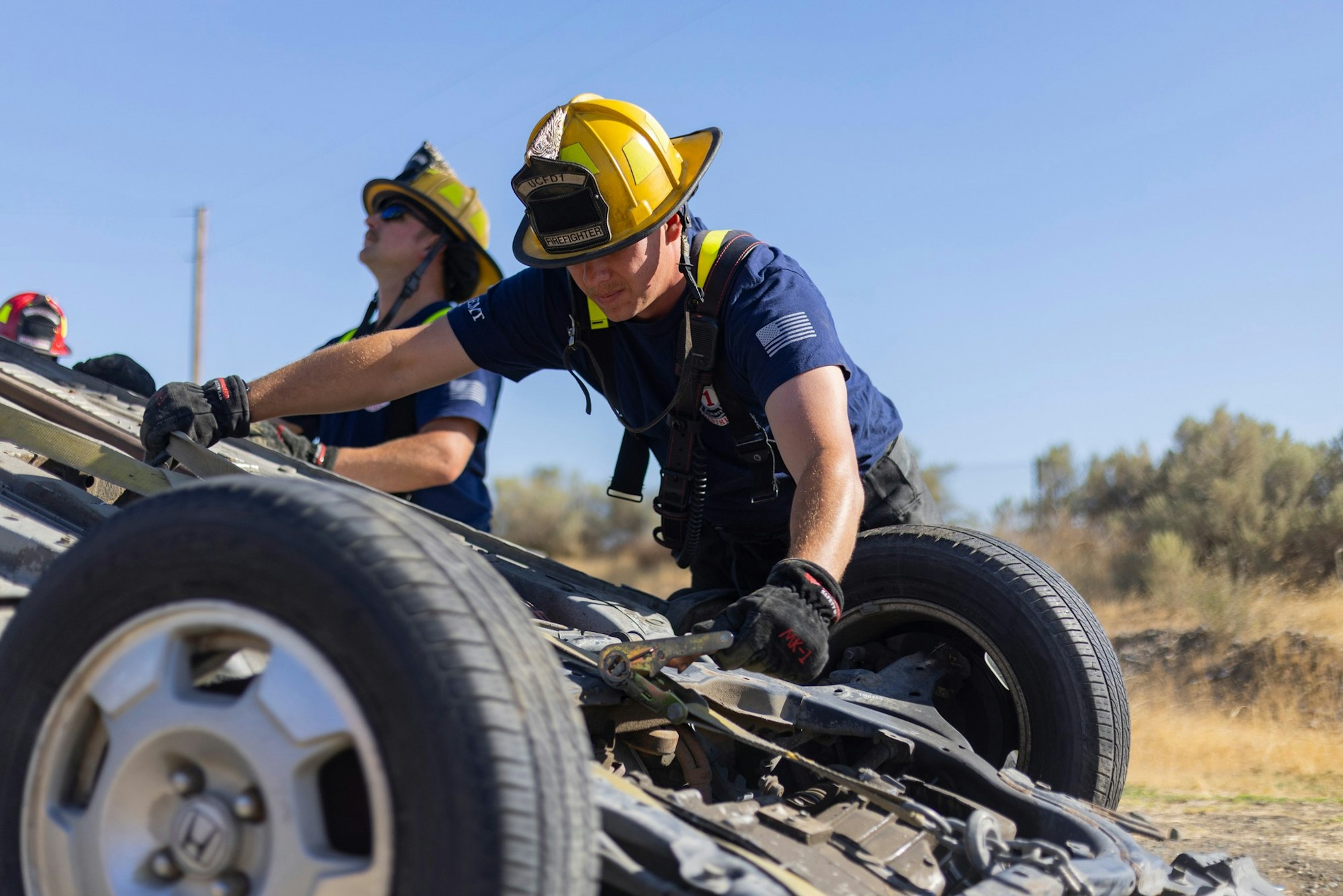Firefighters inspecting an overturned vehicle outdoors.