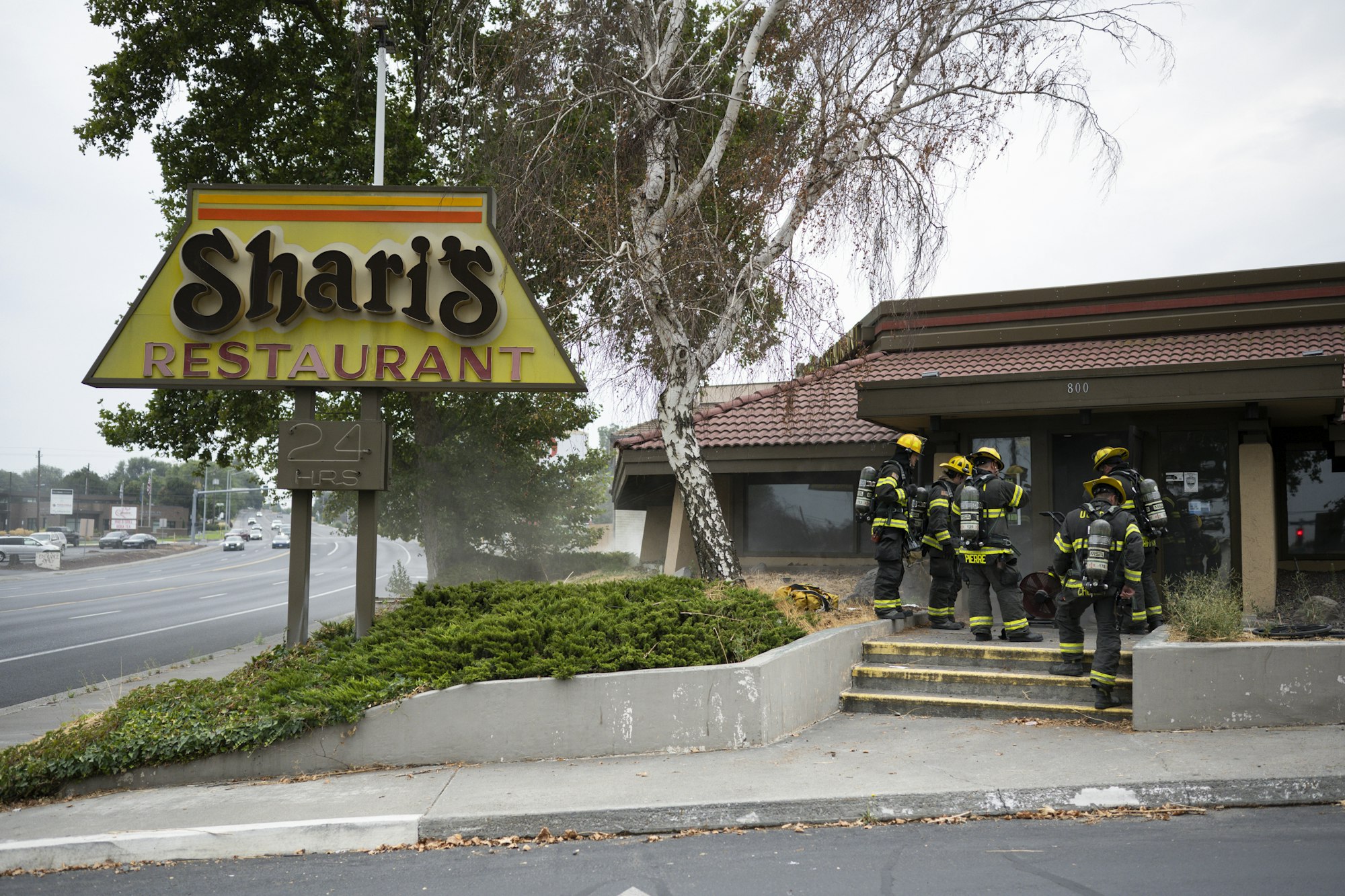 Firefighters outside Shari's Restaurant with gear, near a roadside.