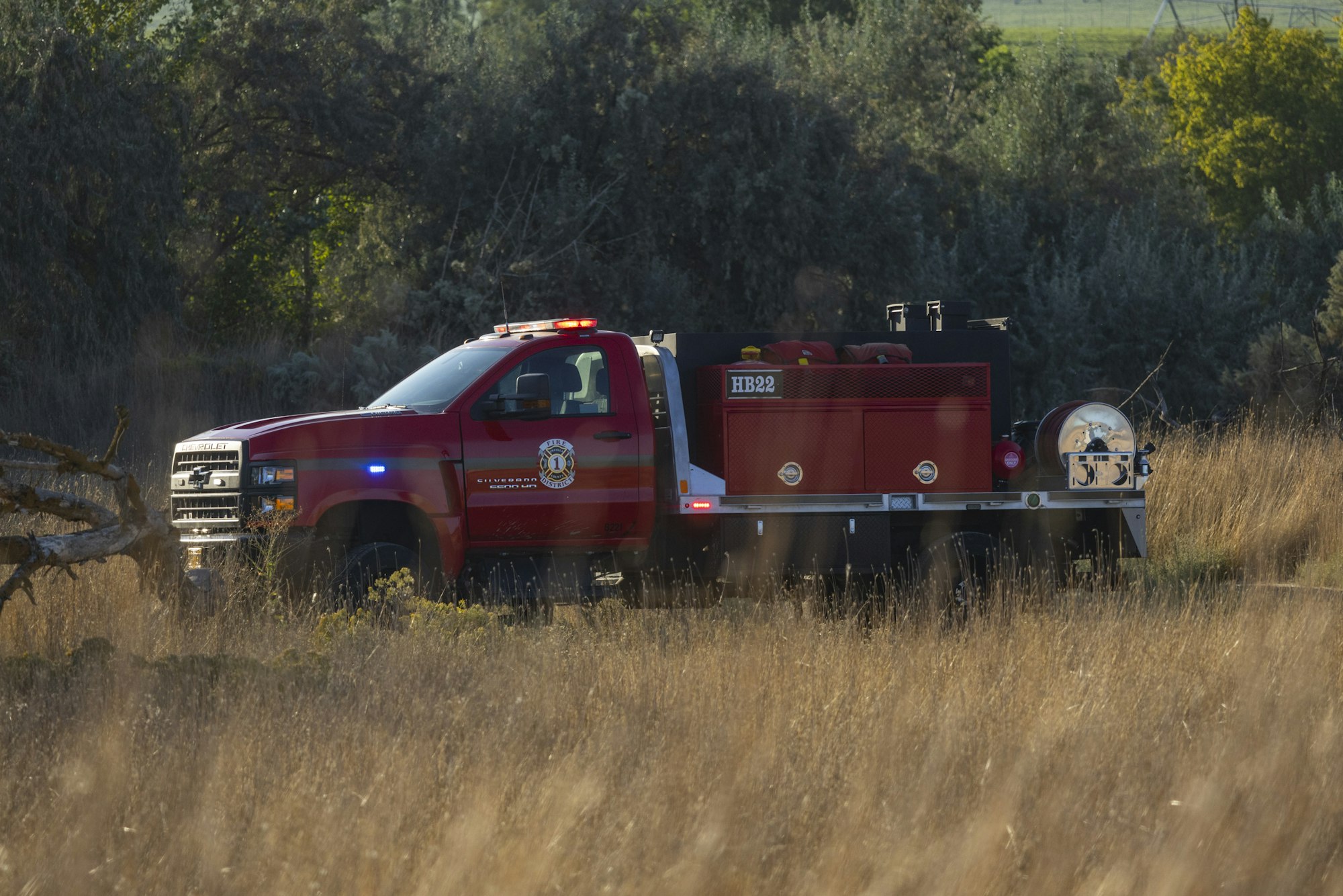 A red fire truck is parked in a field surrounded by trees and grass.