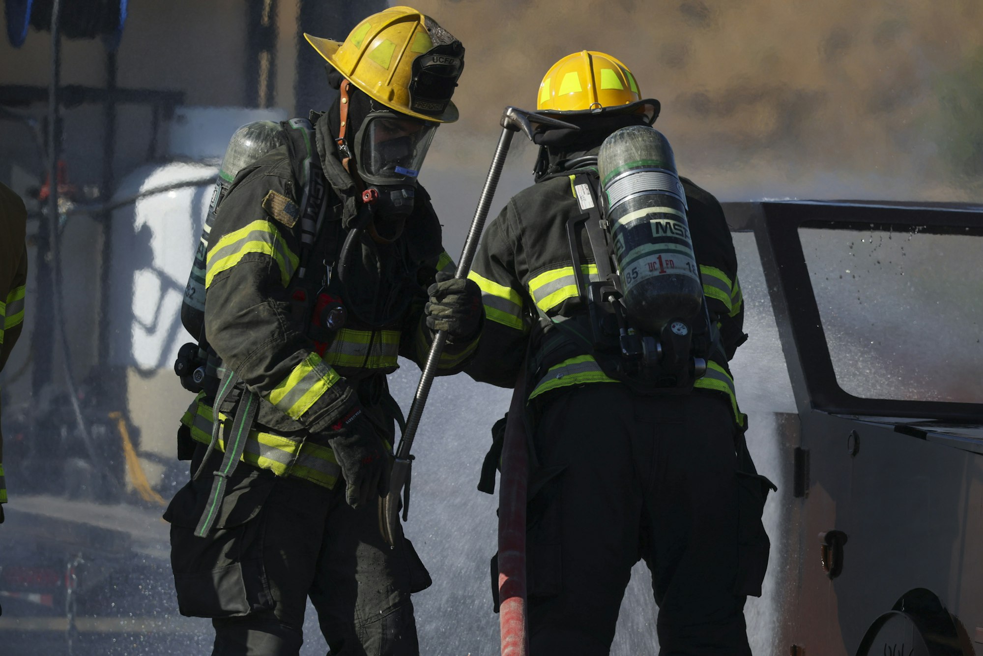 Firefighters in gear using a hose, spraying water at a fire scene.