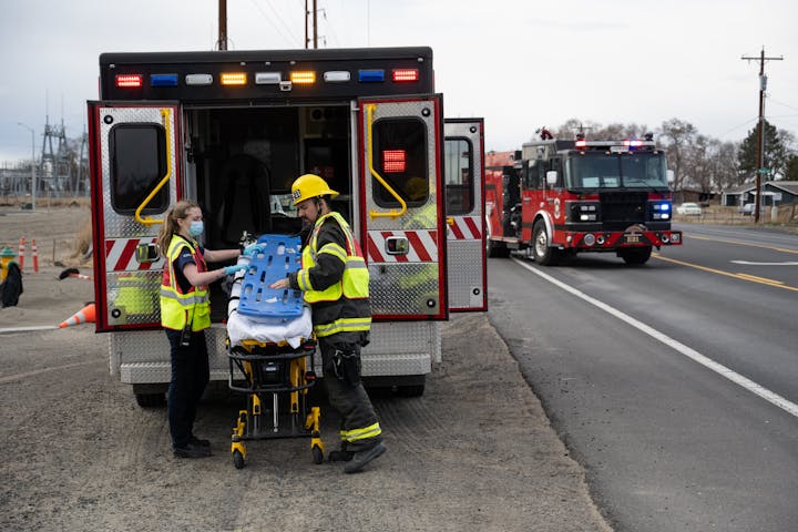 EMTs by an ambulance and a fire truck on a road.