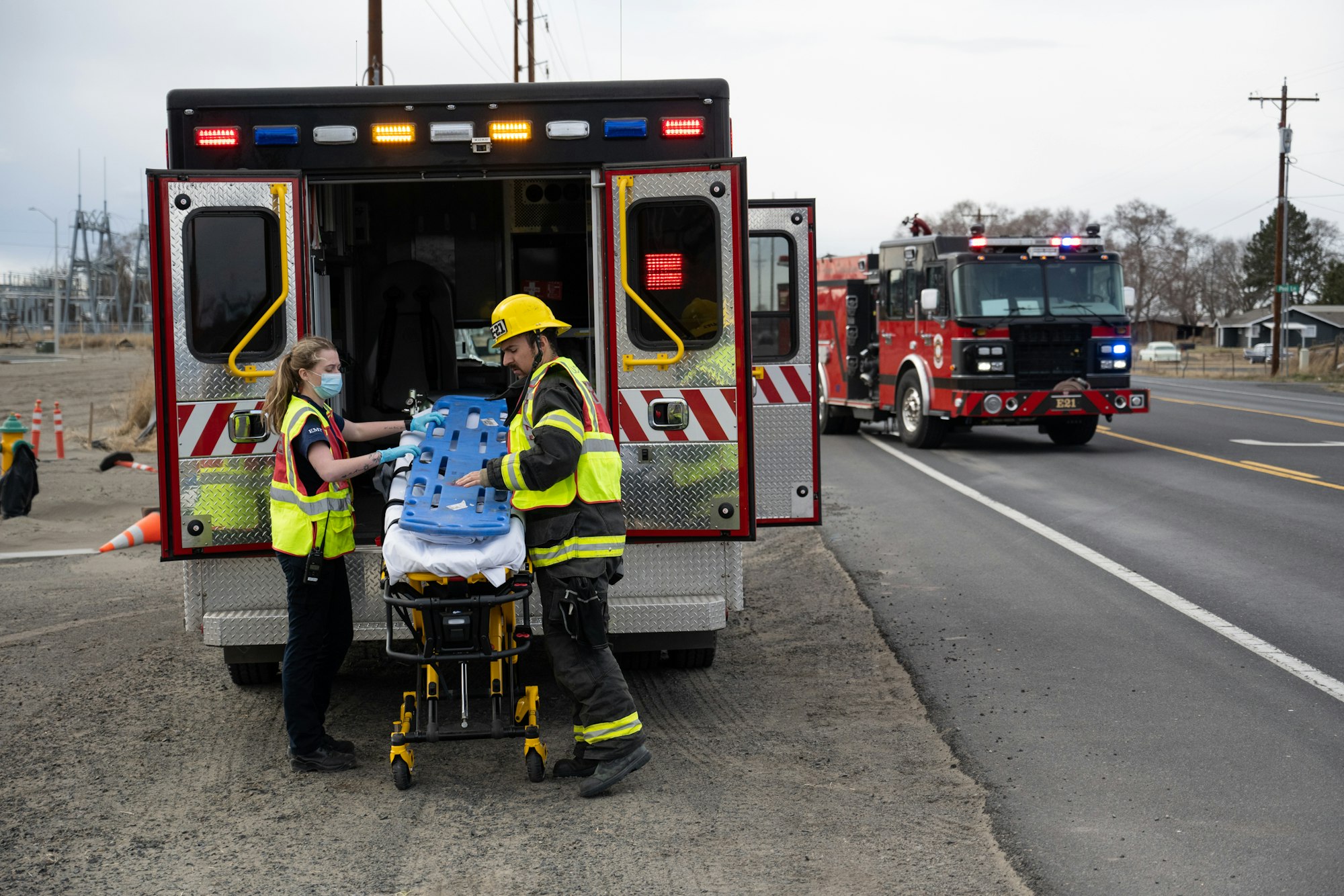 EMTs by an ambulance and a fire truck on a road.