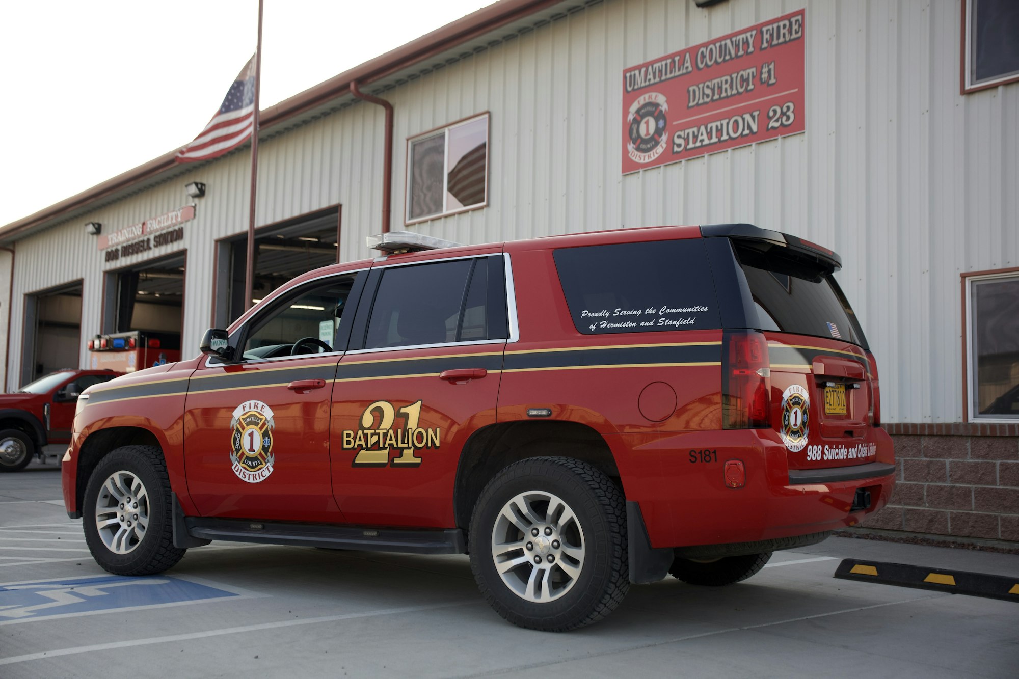 Red fire department SUV marked "Battalion 21" parked outside Umatilla County Fire Station 23, with American flag visible.