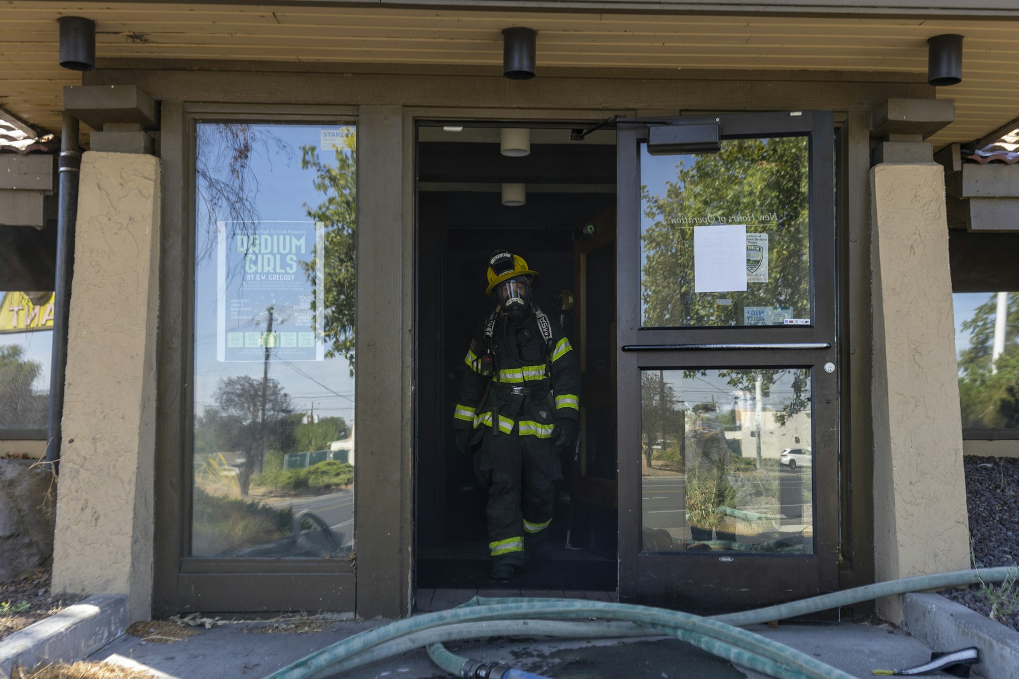 Firefighter in gear enters a building with hoses on the ground.
