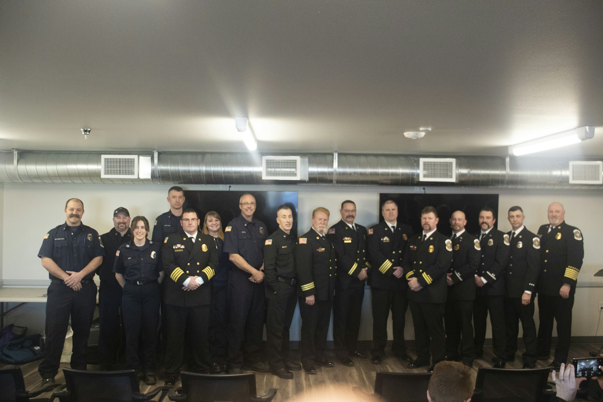 A group of uniformed firefighters and officials posing for a photo indoors.
