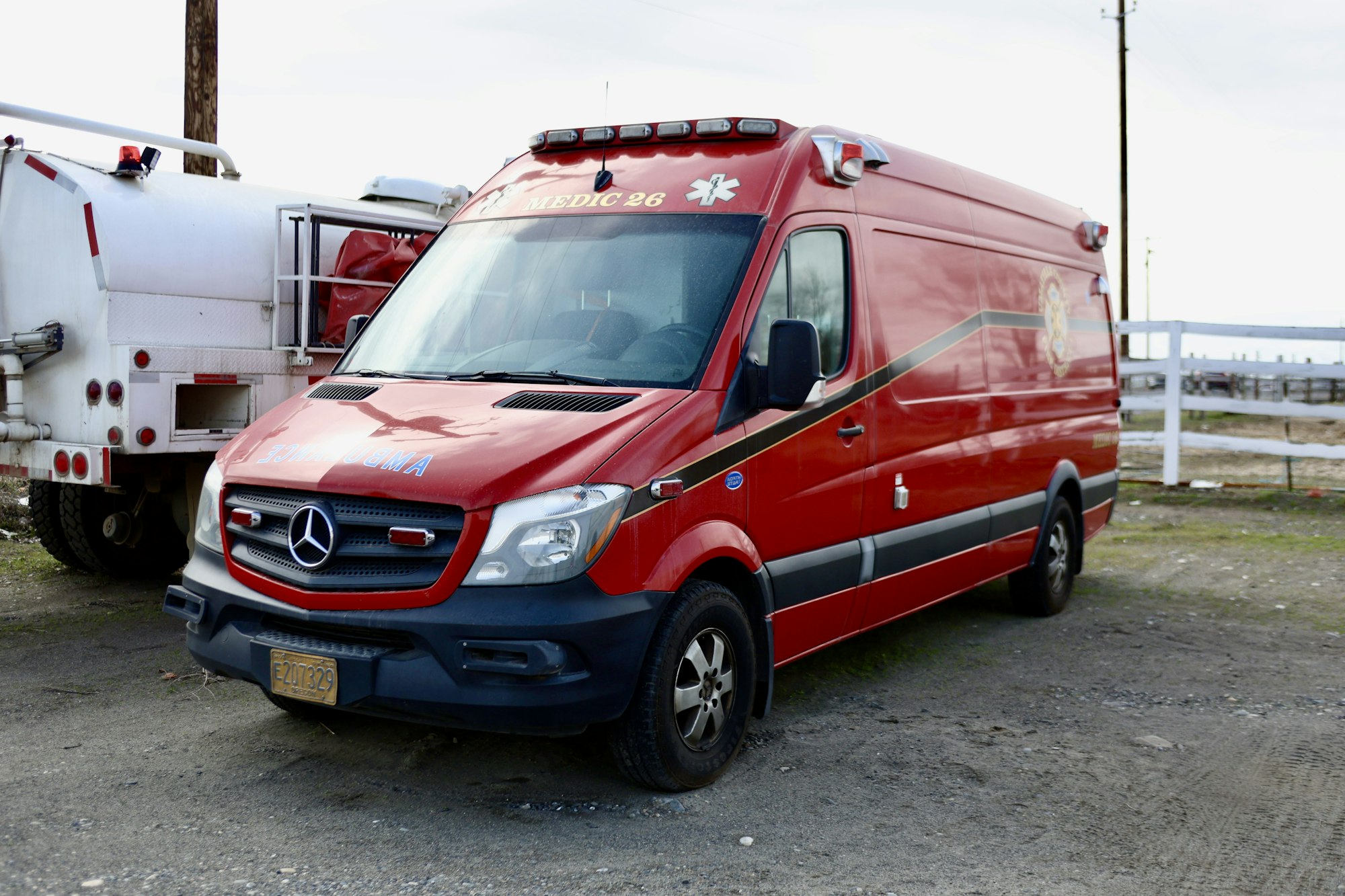 Red Mercedes-Benz ambulance parked beside a white utility truck.
