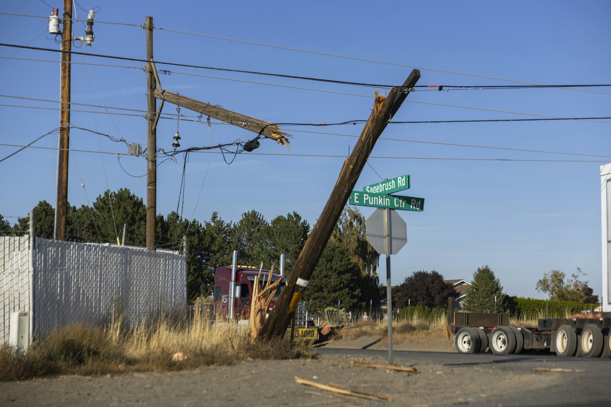Broken utility pole with power lines on road intersection of Sagebrush Rd and E Punkin Center Rd, semi-truck nearby.