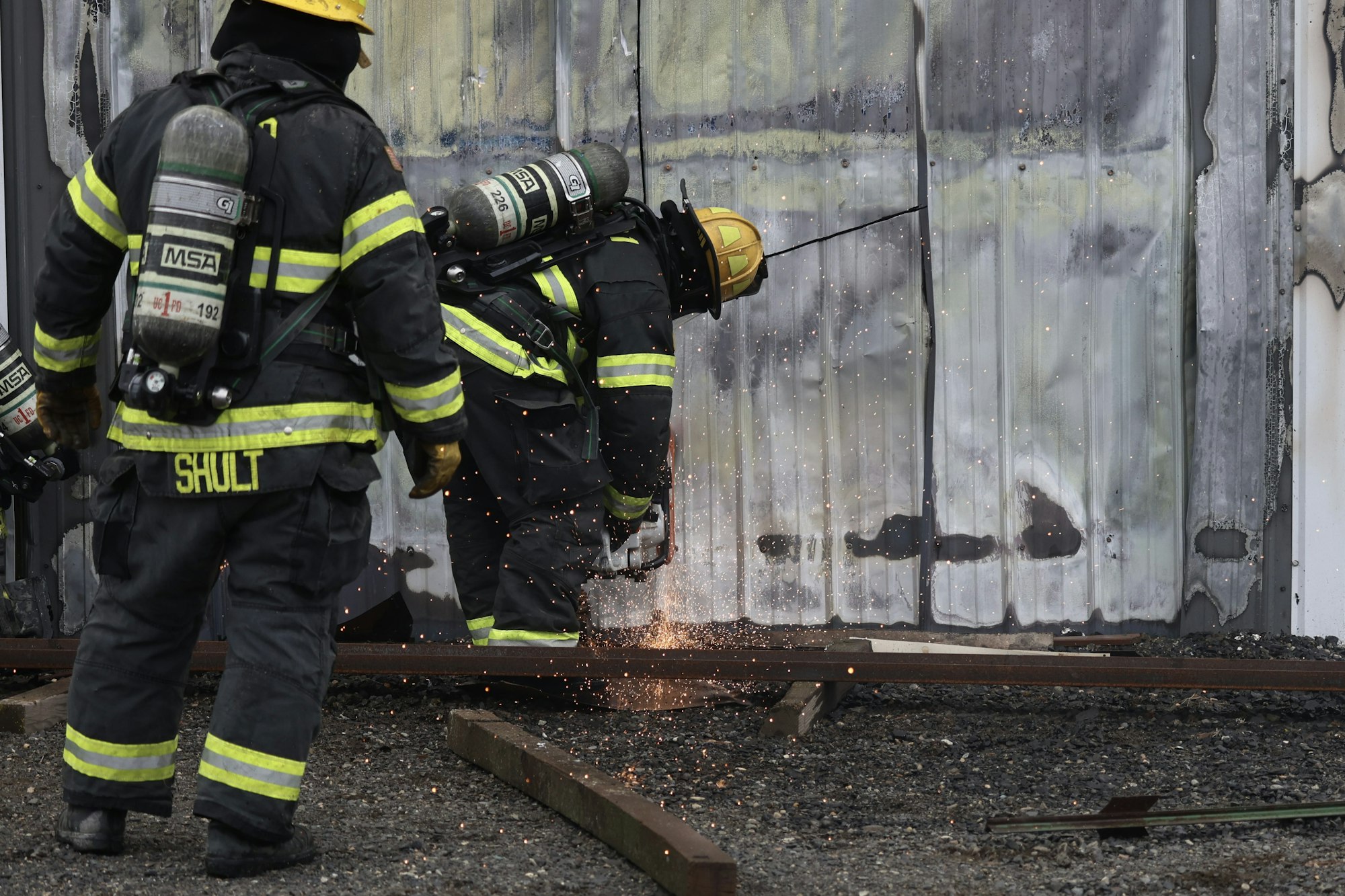 Firefighters in gear cutting a metal door with sparks flying.