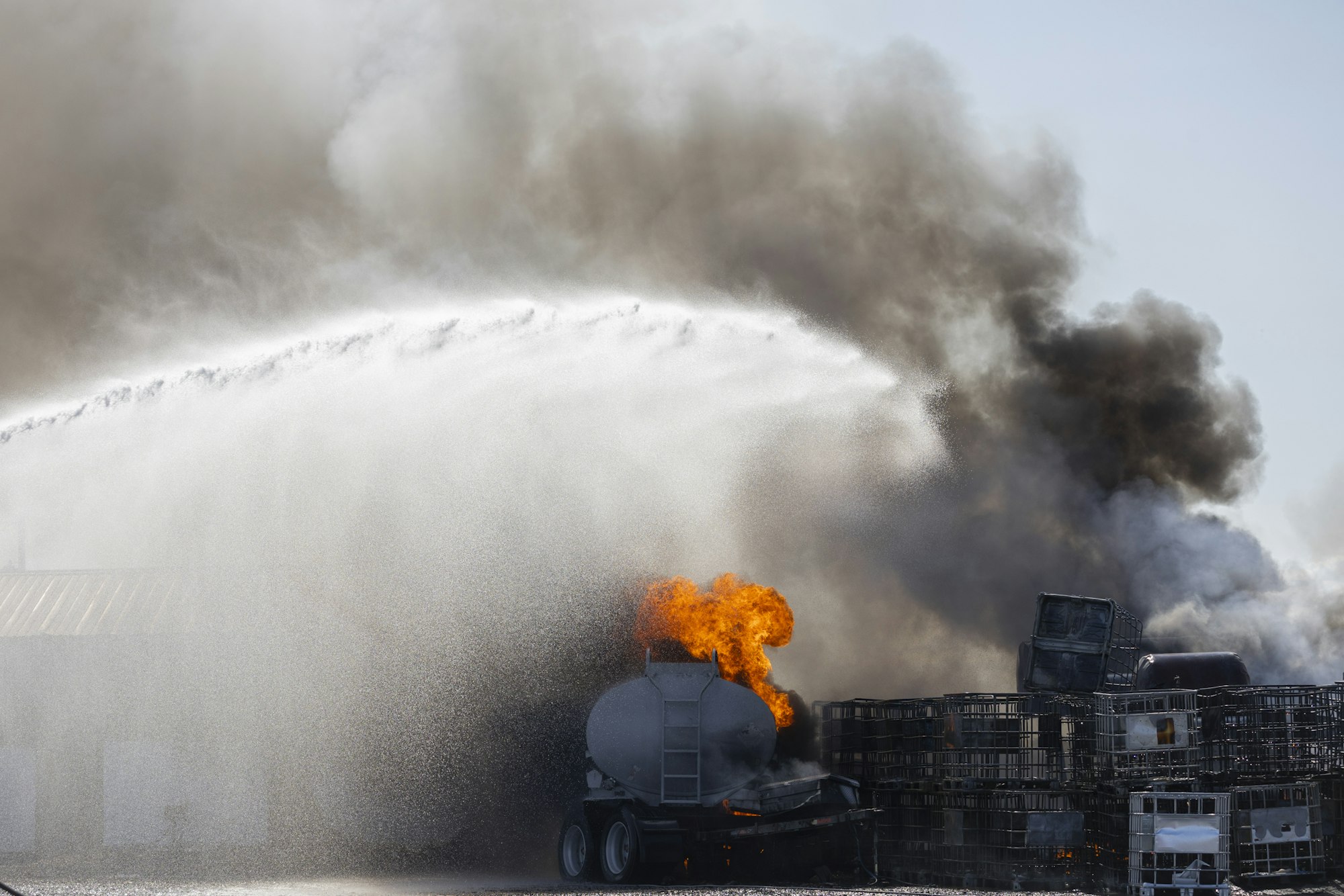 Firefighting operation on a burning vehicle with heavy smoke and water spray.