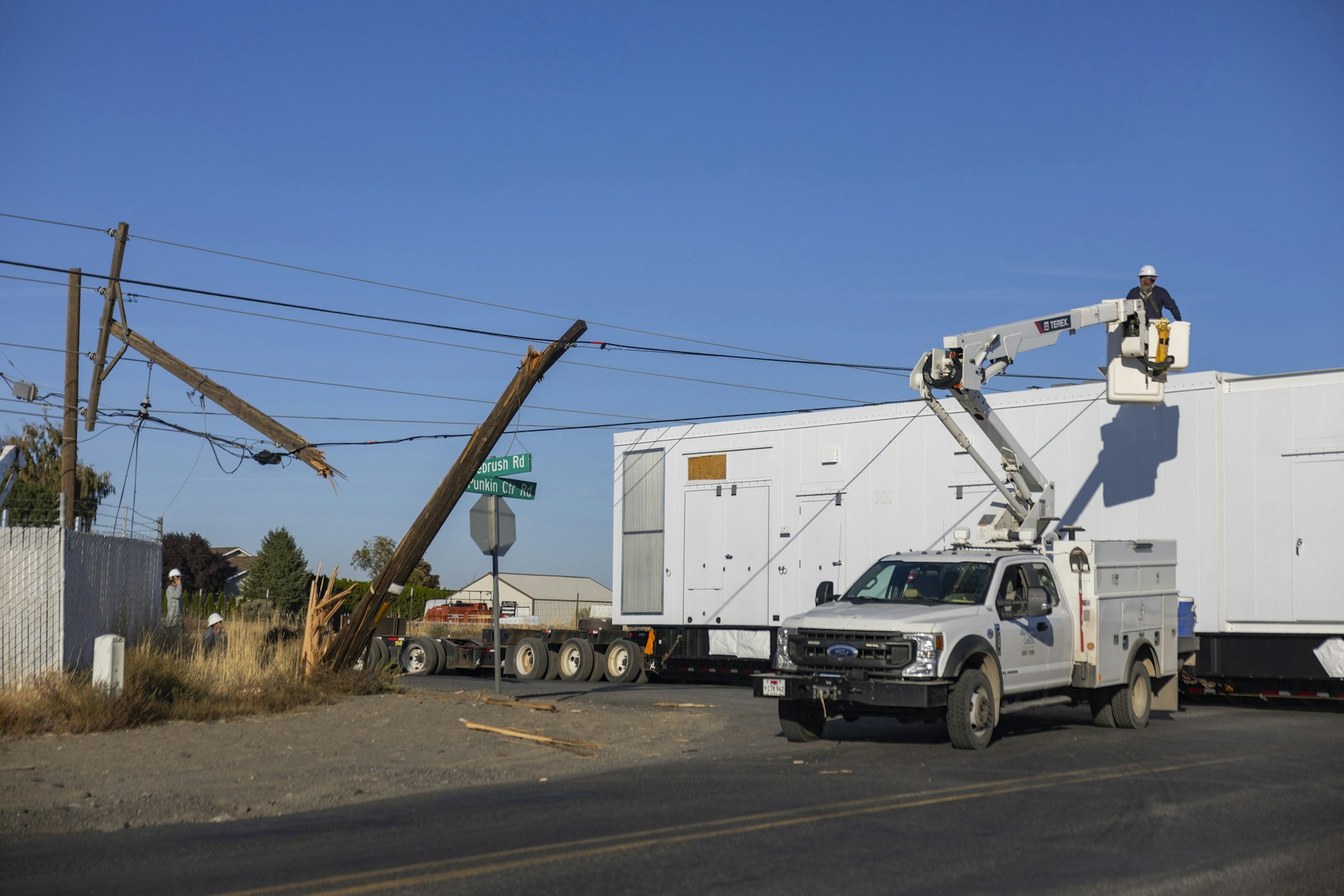 Utility workers repairing fallen power lines and broken pole with a truck-mounted boom lift at an intersection.