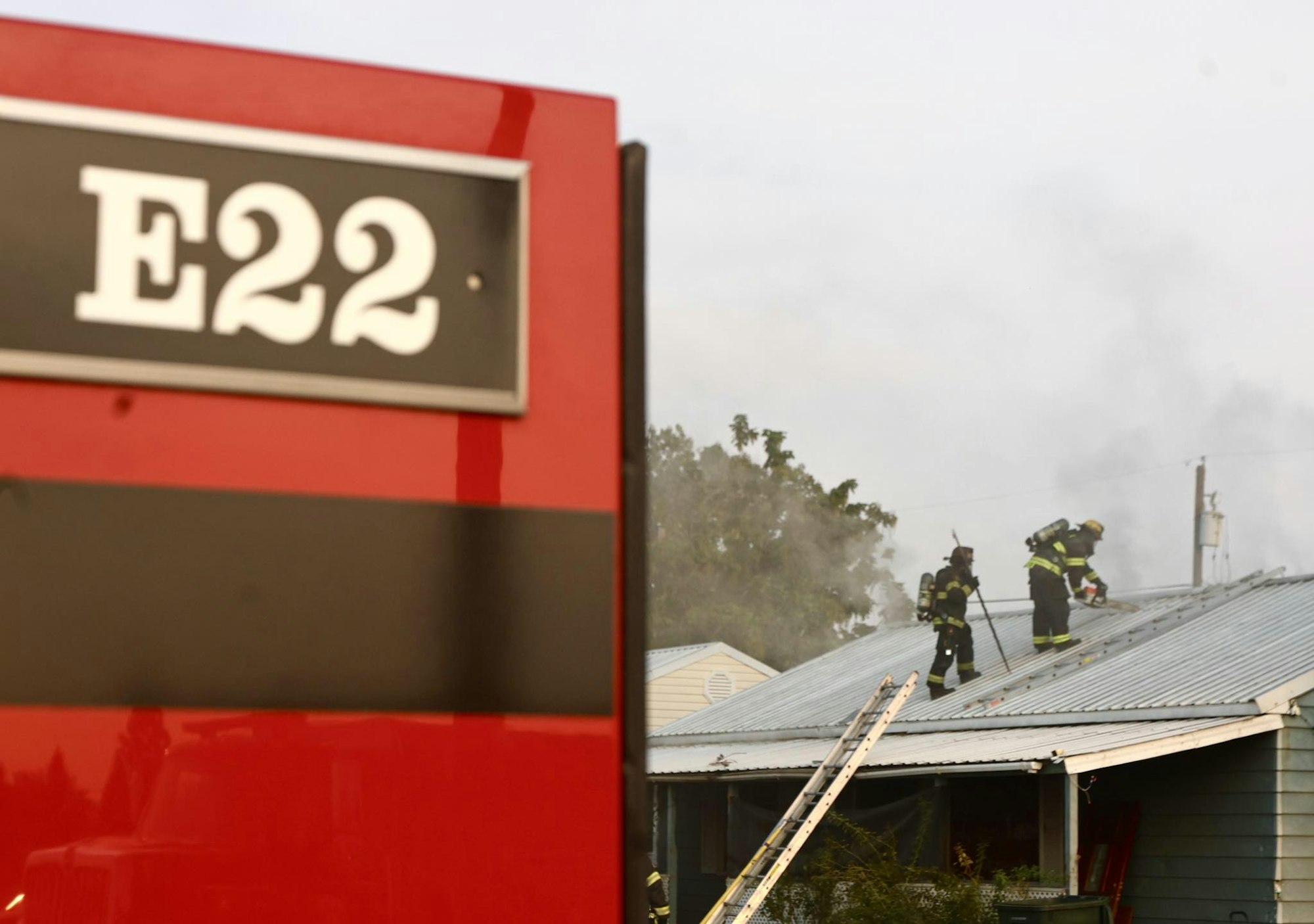 Firefighters on a roof; red fire truck with "E22" visible in the foreground.