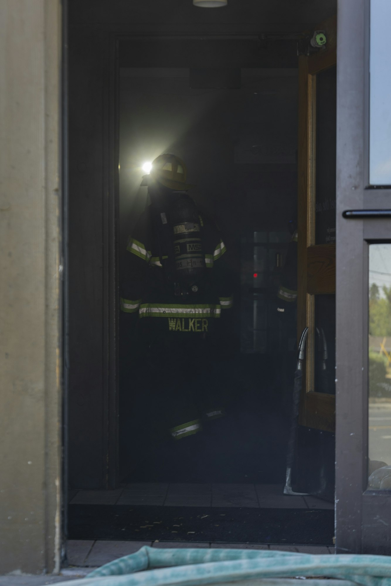 Firefighter entering a dark, smoky building with equipment and a spotlight.