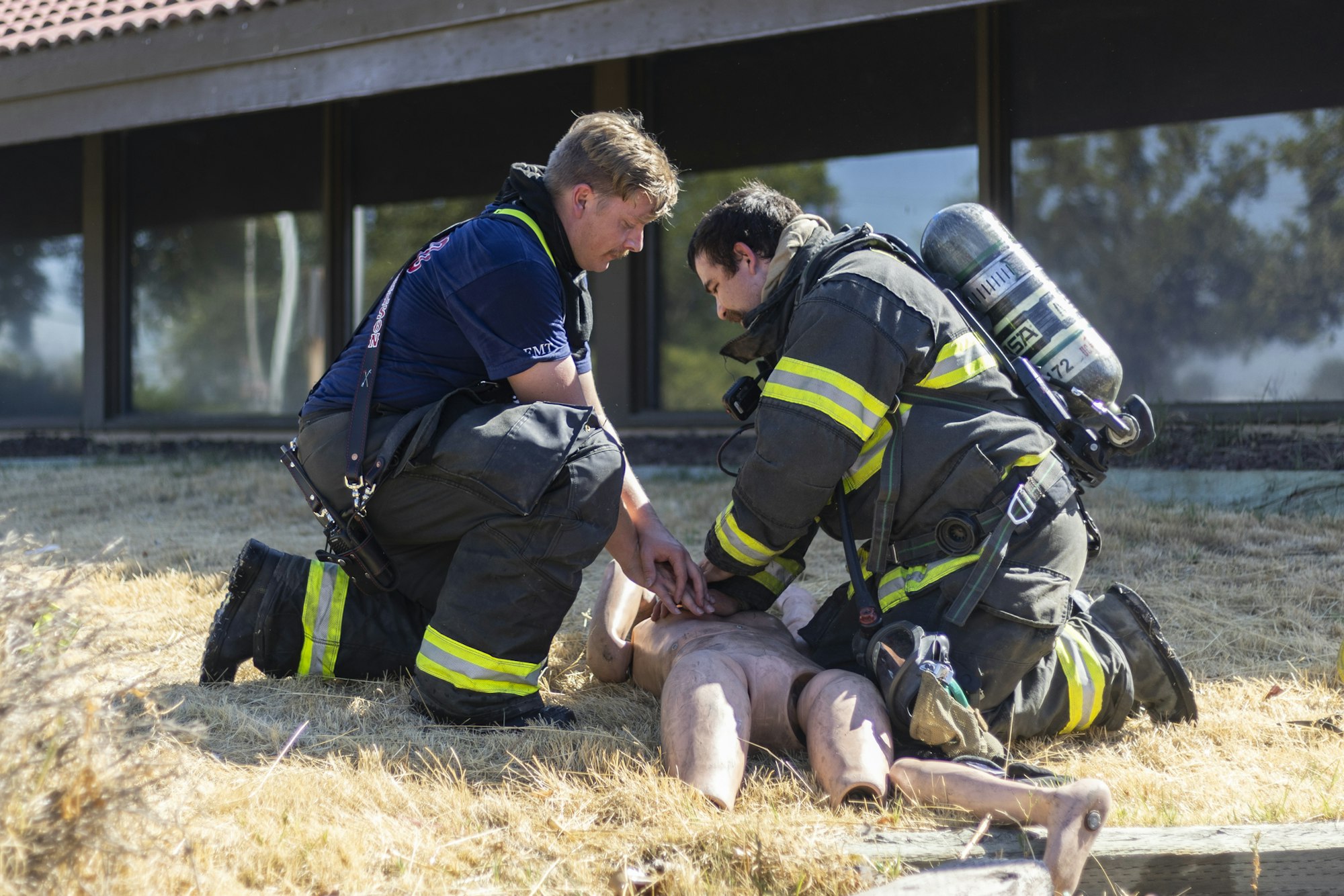 Two firefighters practicing CPR on a training dummy outside.