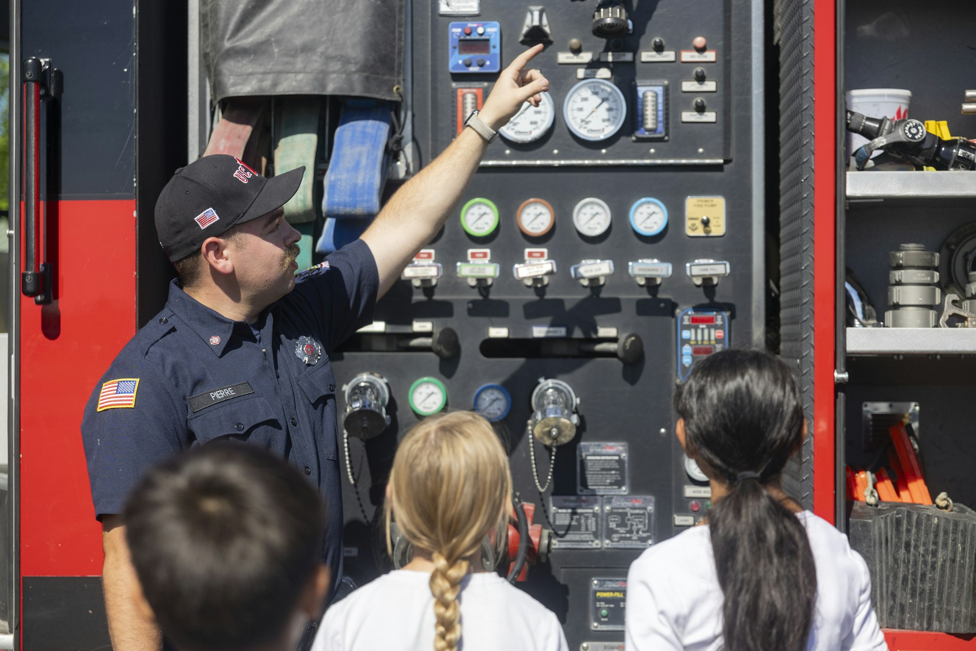 A firefighter explains equipment on a fire truck to a group of children.