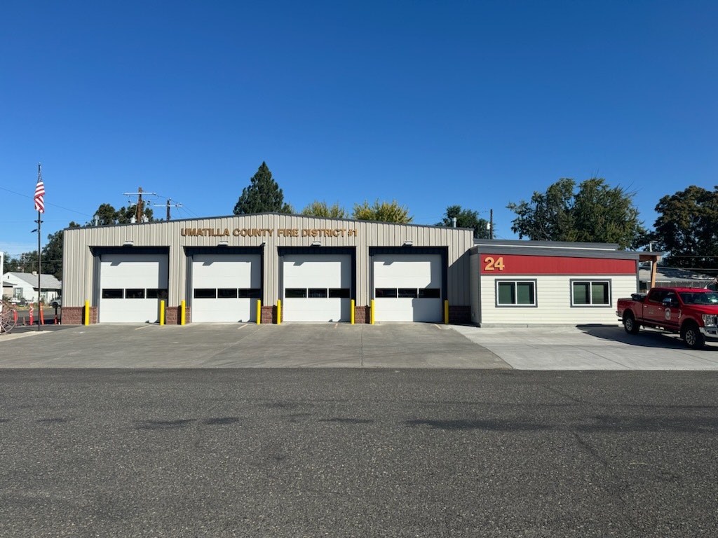 A fire station with three garages and a red truck parked outside under a clear blue sky.