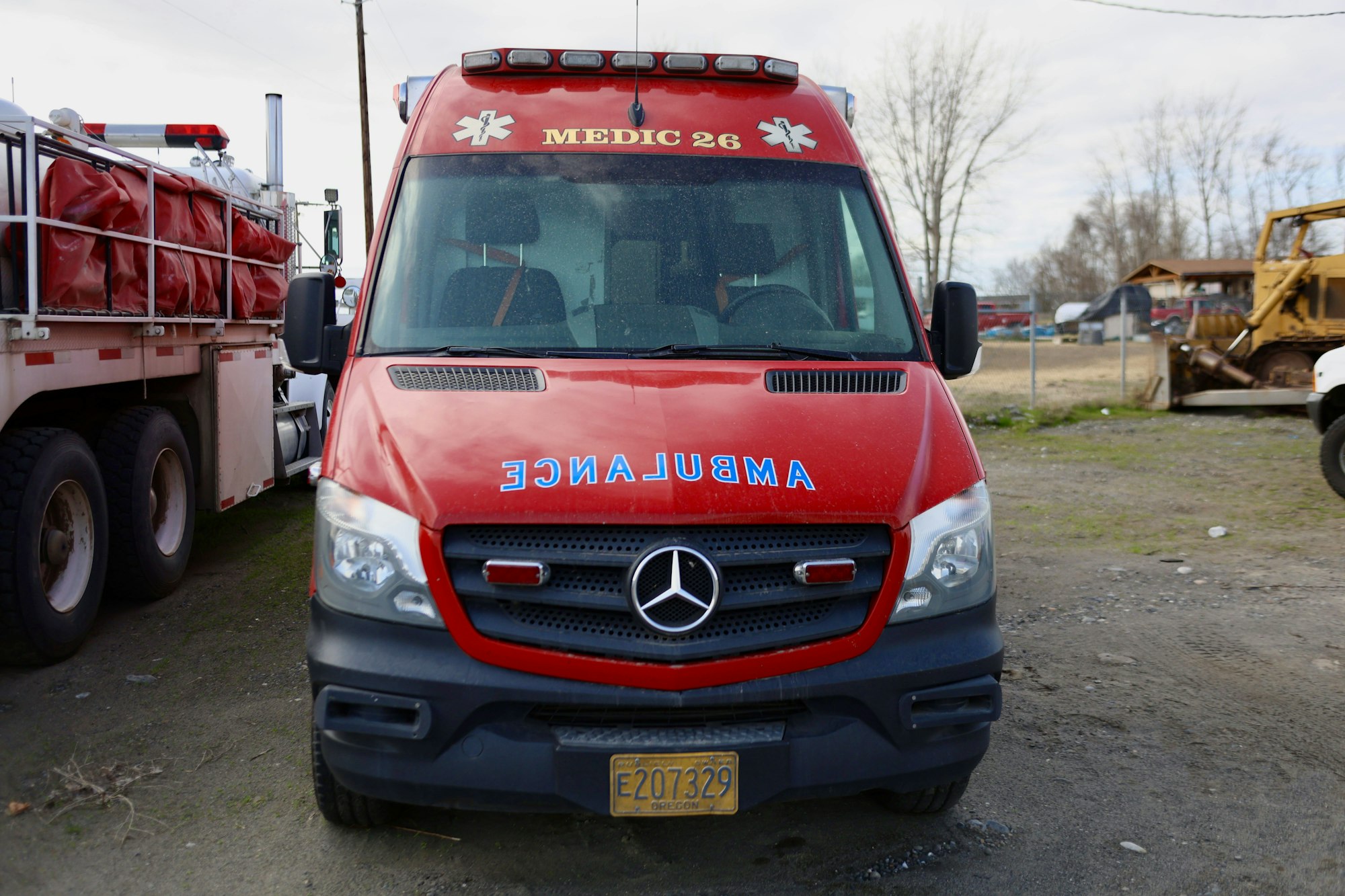 Red ambulance with "AMBULANCE" written backward on the hood, parked in a lot.