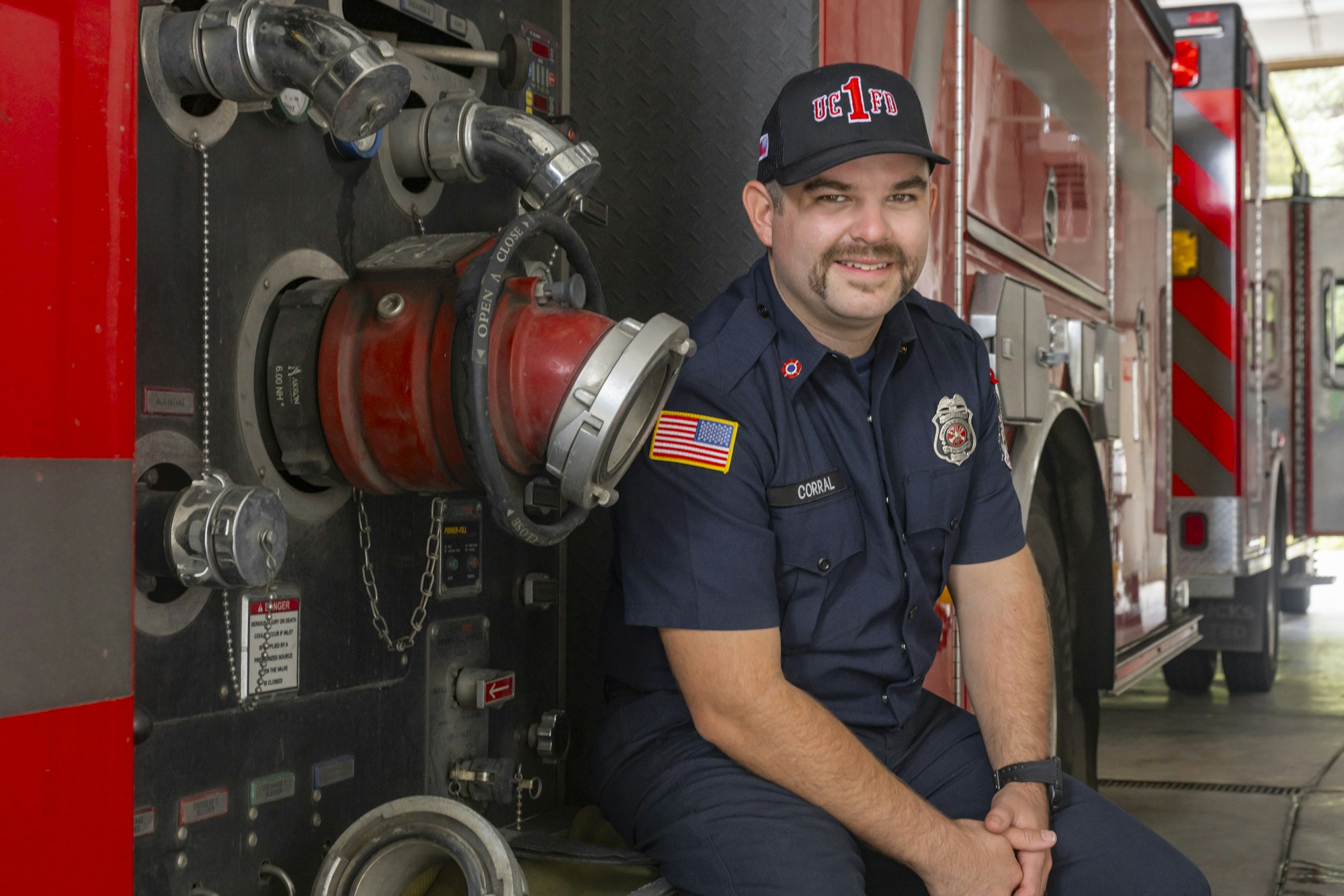 A firefighter sitting next to a fire truck, wearing a uniform and cap.