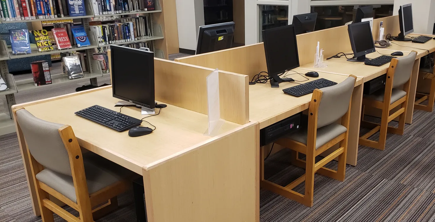 A library with computers, partition walls, chairs, and bookshelves with books and DVDs.